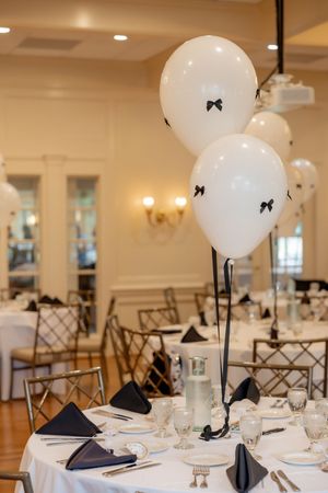 Elegant bridal shower venue with white balloon centerpieces featuring black bows and navy napkins.
