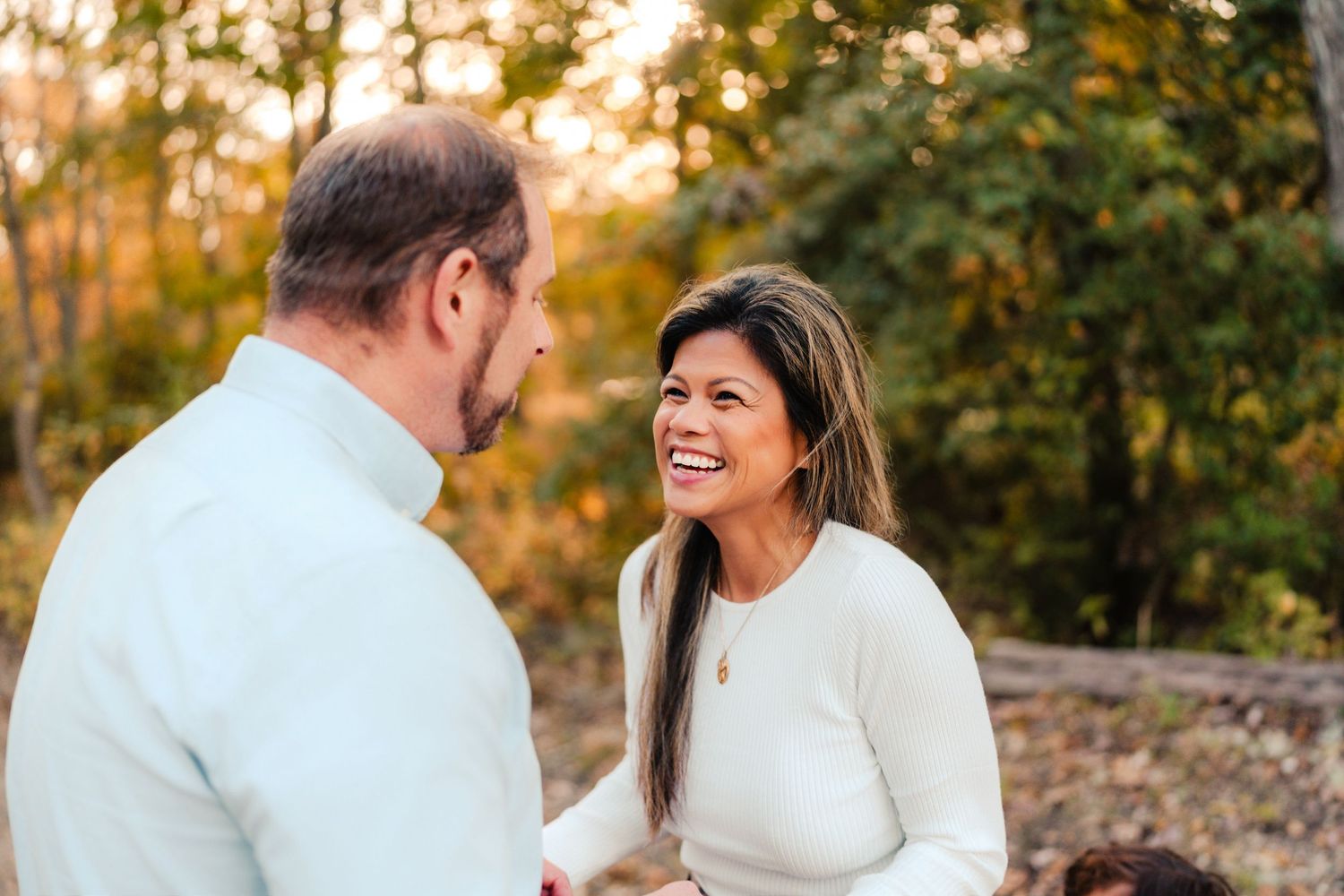 Couple in white outfits sharing romantic moments during golden hour photoshoot in autumn forest setting.