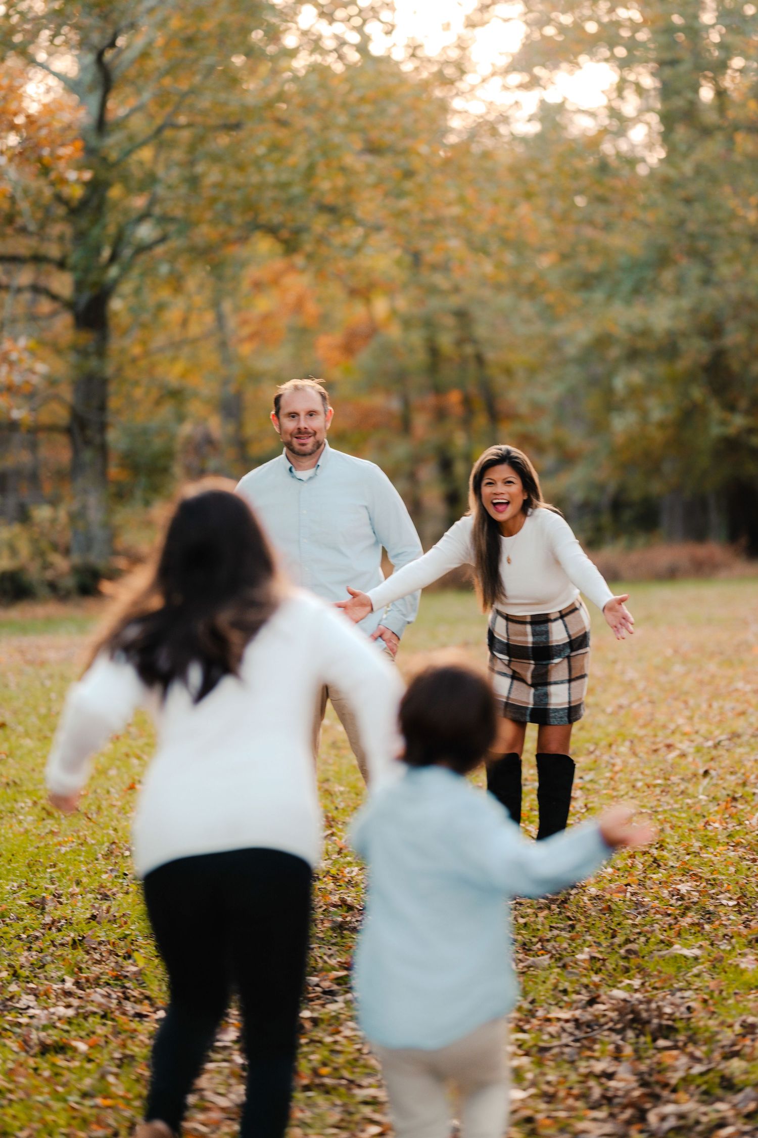 A playful family enjoys a fall day together throwing autumn leaves in a park setting with golden foliage.