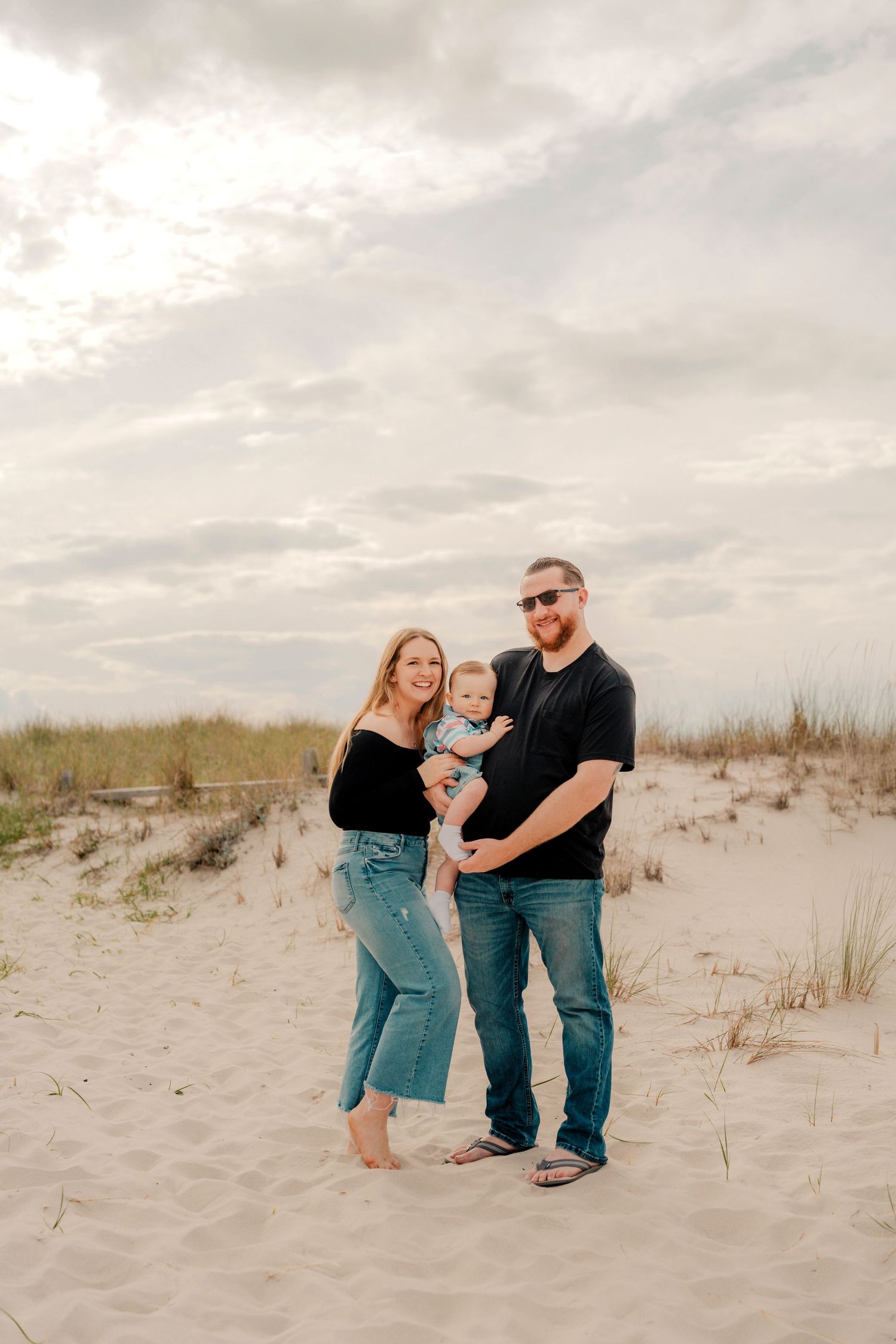 Family enjoys a tender moment together while sitting on coastal sand dunes at sunset.