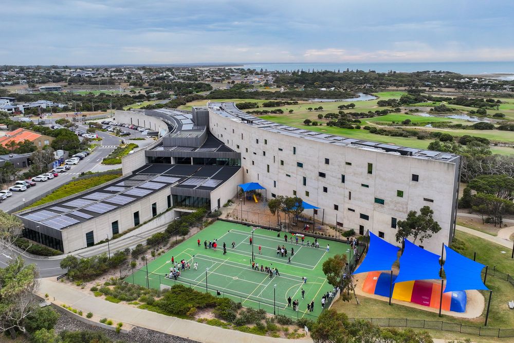 Aerial view of sports facilities showing green courts, colorful structures, and surrounding coastal urban landscape.