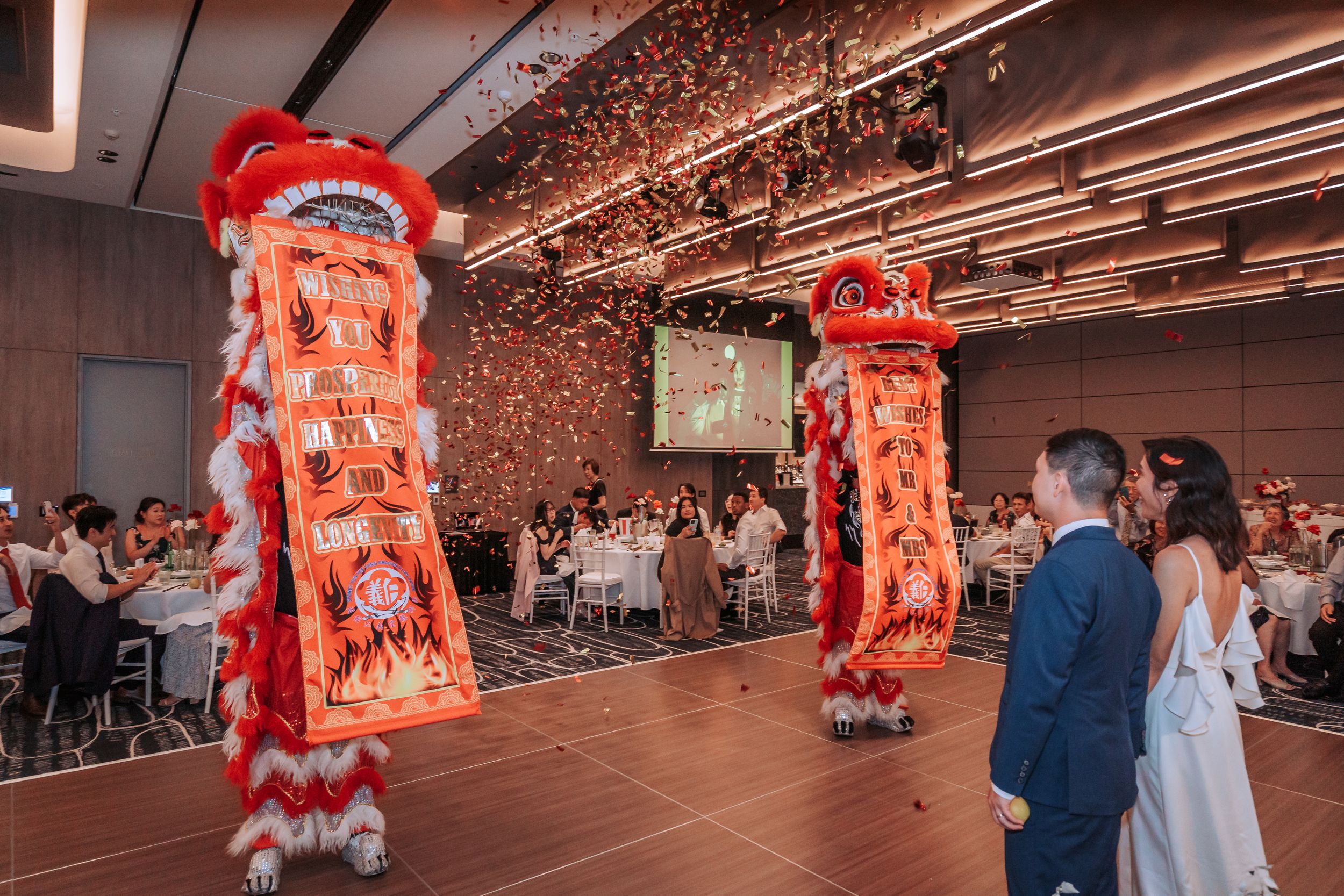 Vibrant lion dance performance with red and gold costumes entertaining wedding guests in a reception hall.