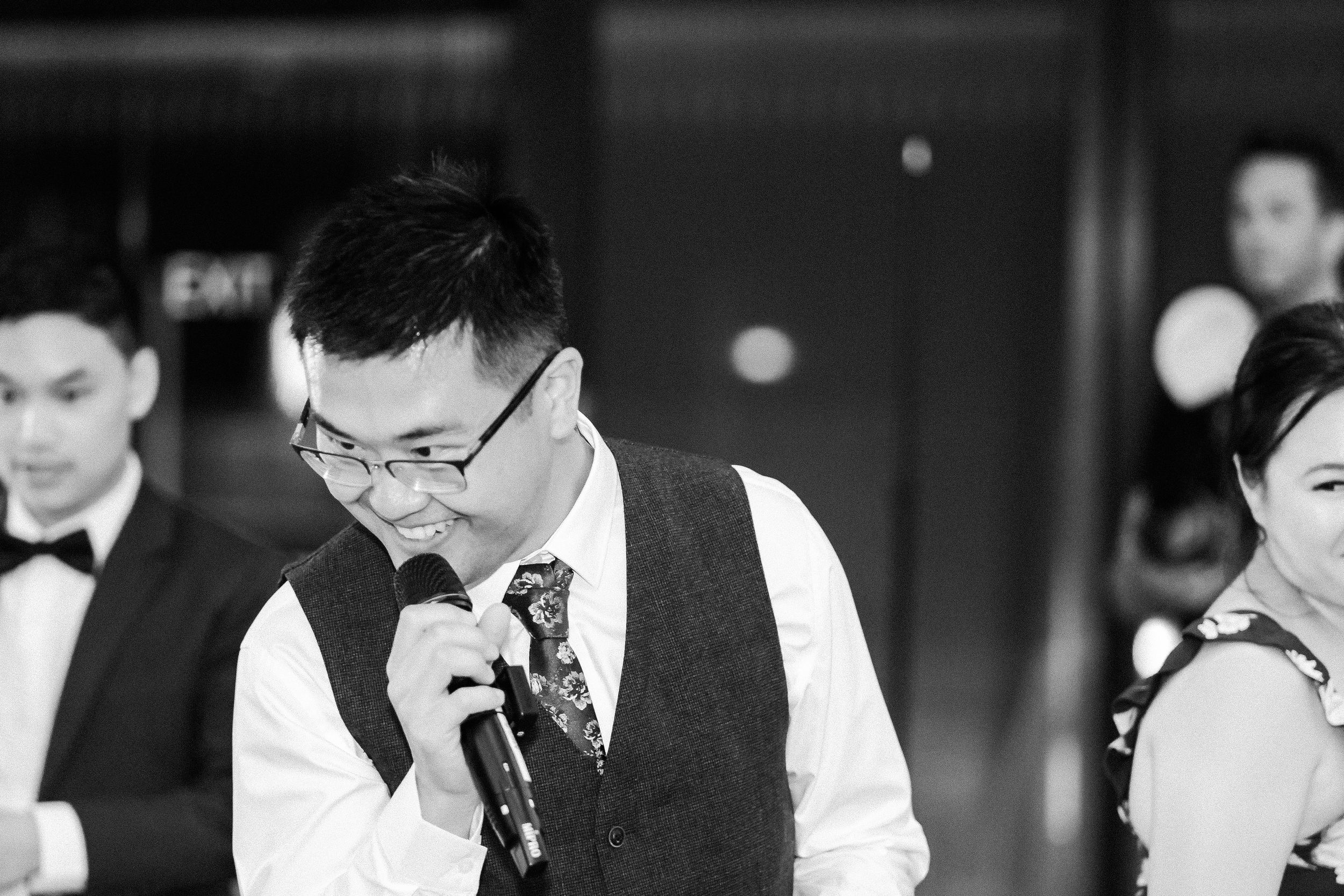 Person in formal attire giving a speech during wedding reception celebration.