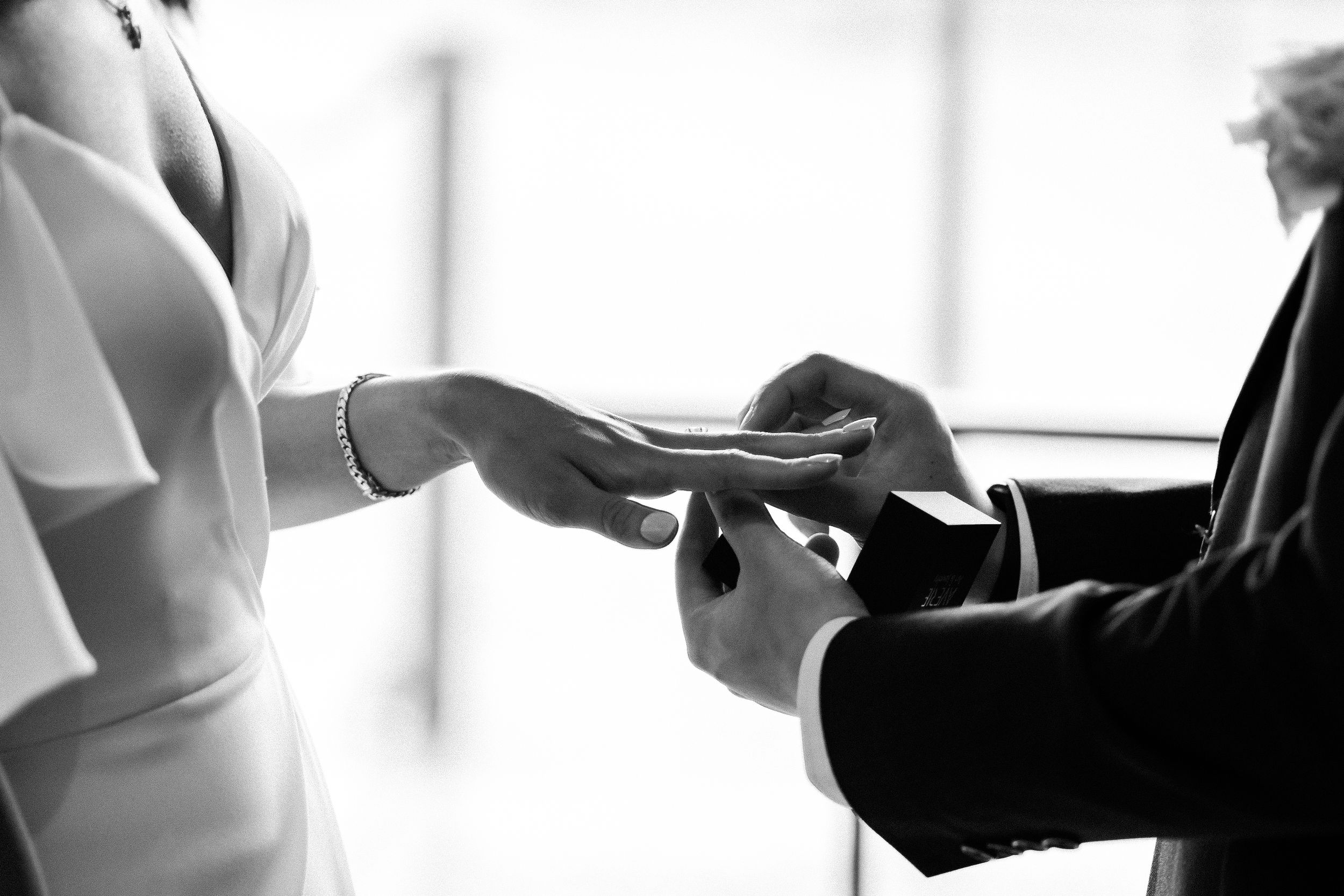 Black and white image capturing intimate ring exchange moment during wedding ceremony.