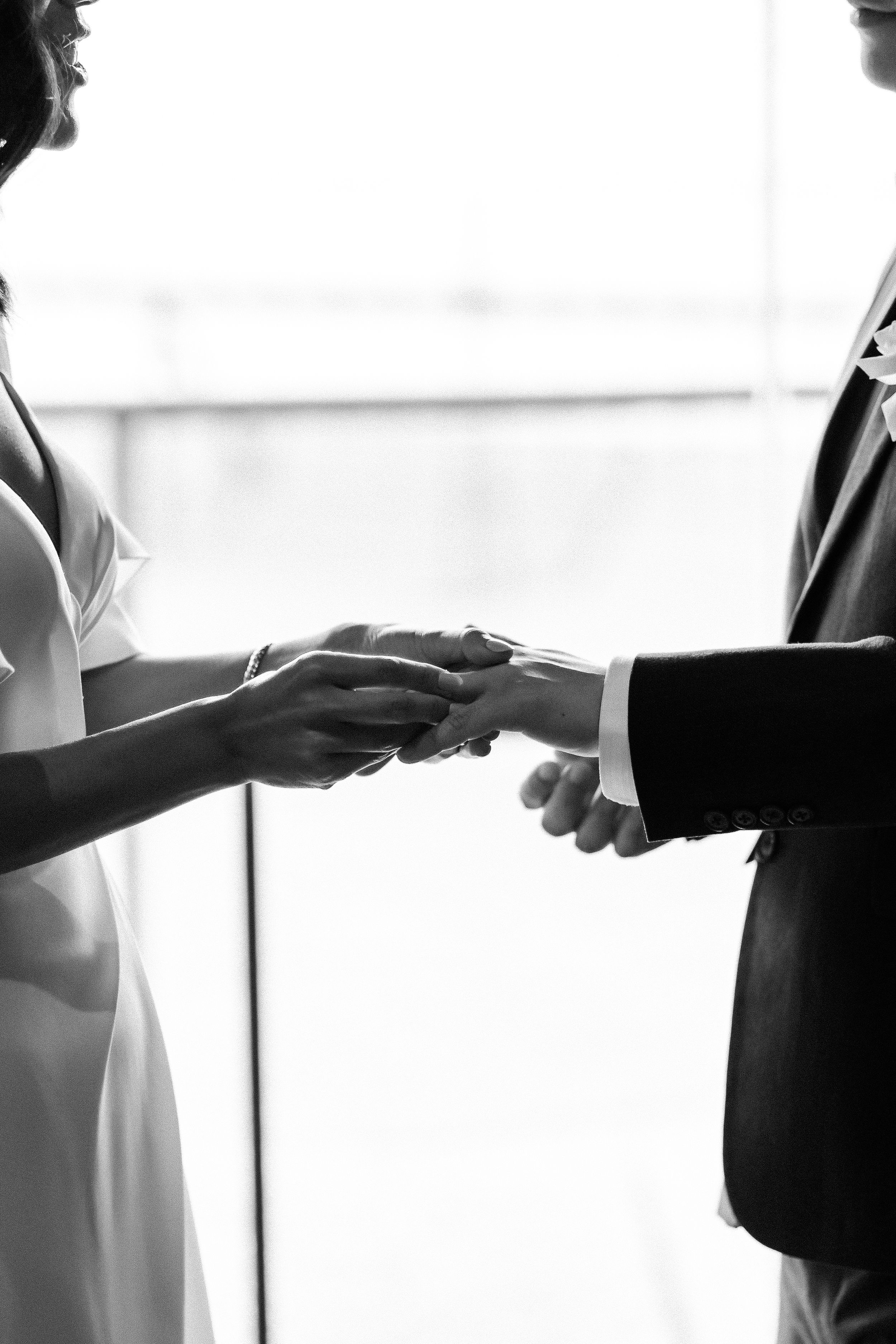 Intimate black and white photo of couple exchanging rings during wedding ceremony.