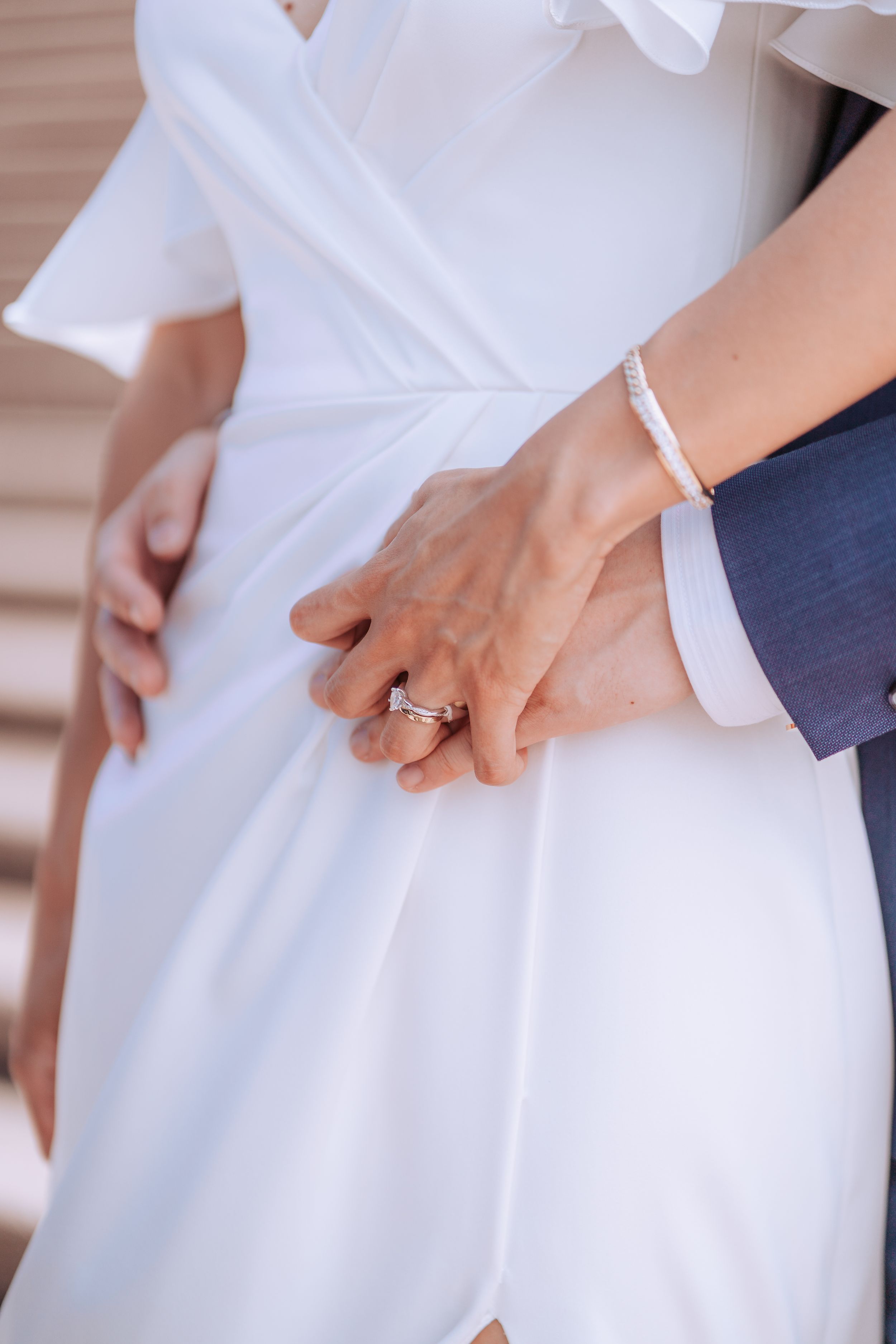 Close-up of newlyweds holding hands showing engagement ring and white wedding dress details.