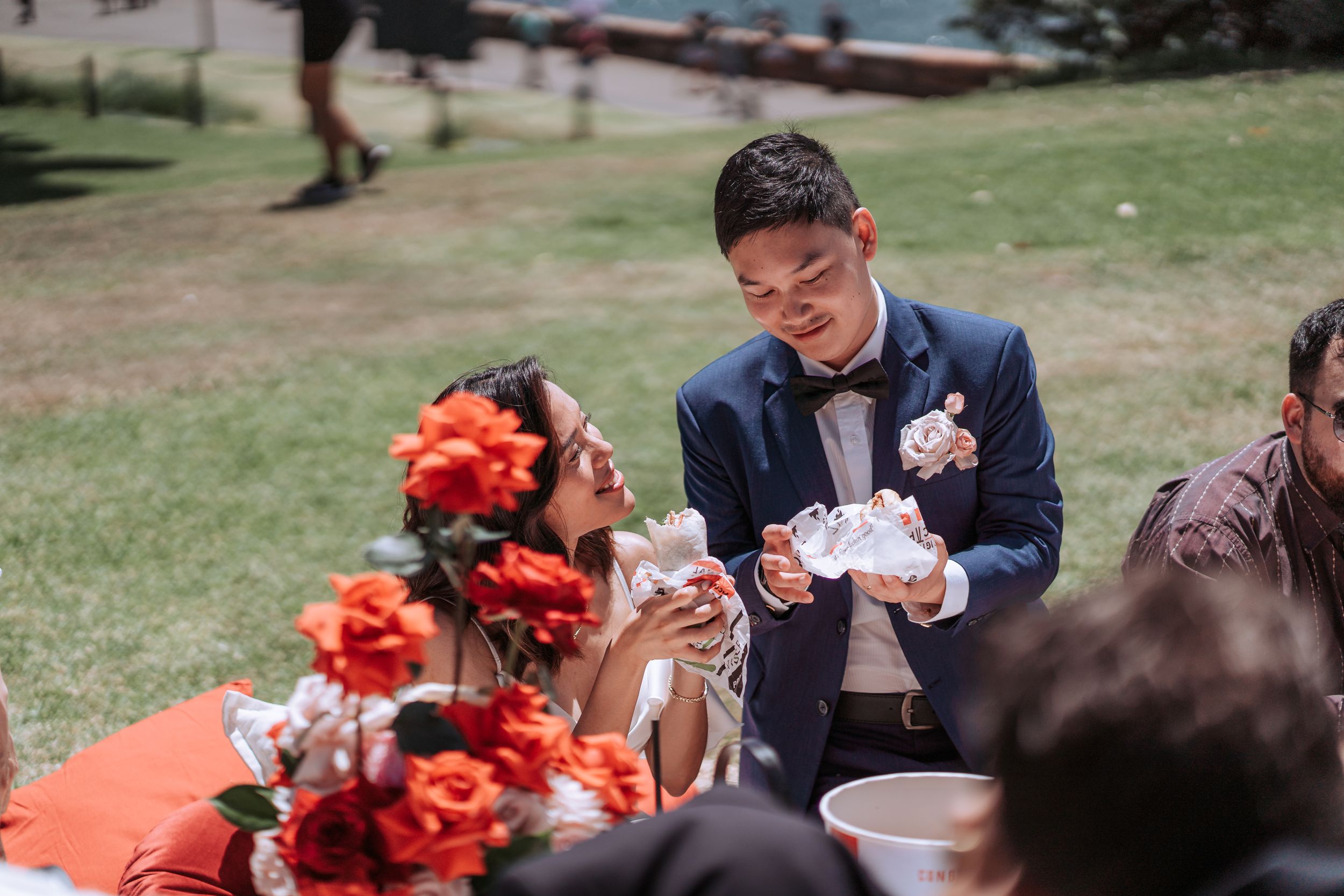 Wedding guest enjoying food at outdoor reception with red floral decorations.