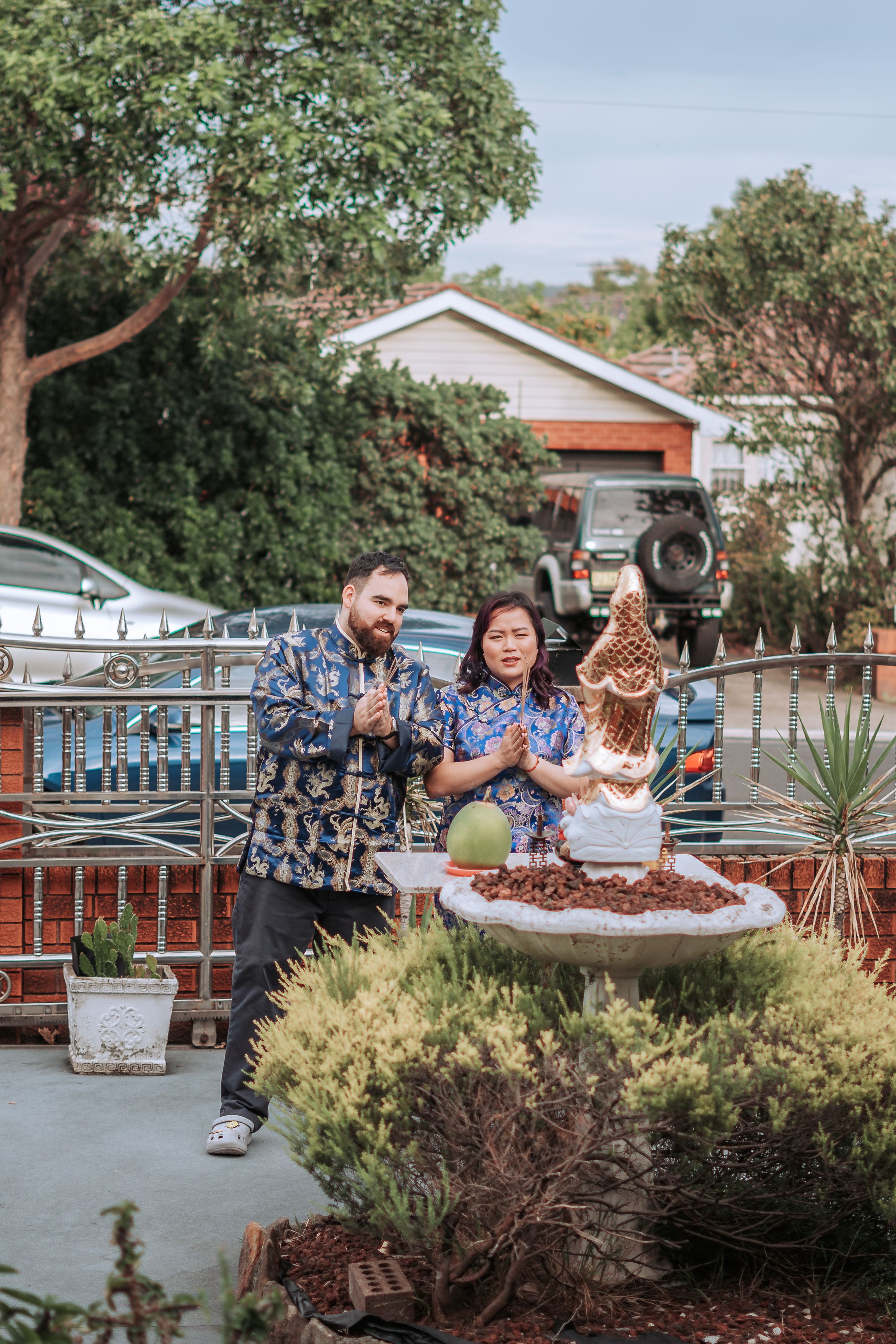 Three people celebrating around a traditional Chinese dessert table in an outdoor garden setting.