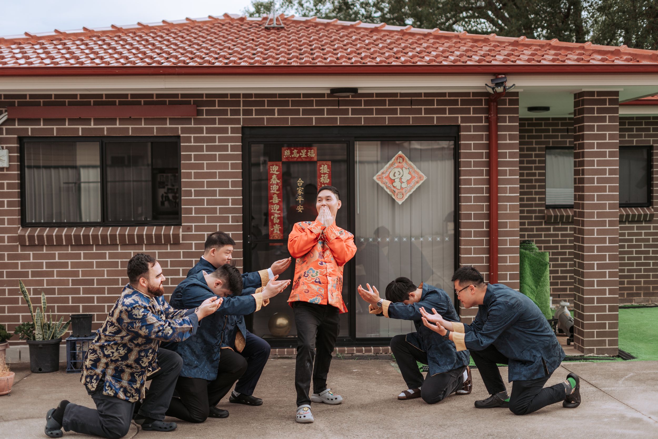 A celebratory moment captured outside a brick house with traditional Chinese decorations.