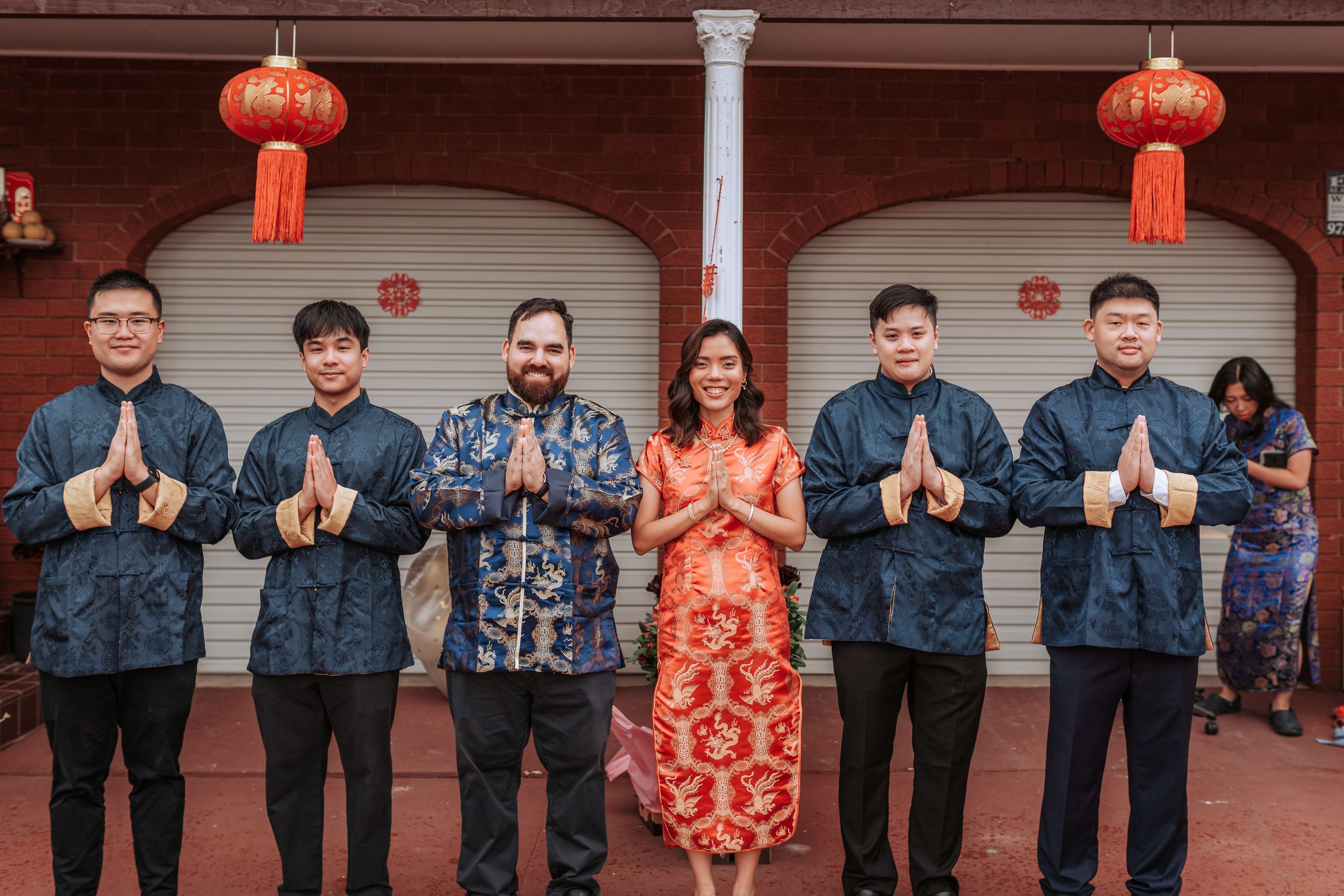 Wedding party in Chinese traditional attire posing with red lanterns in background.