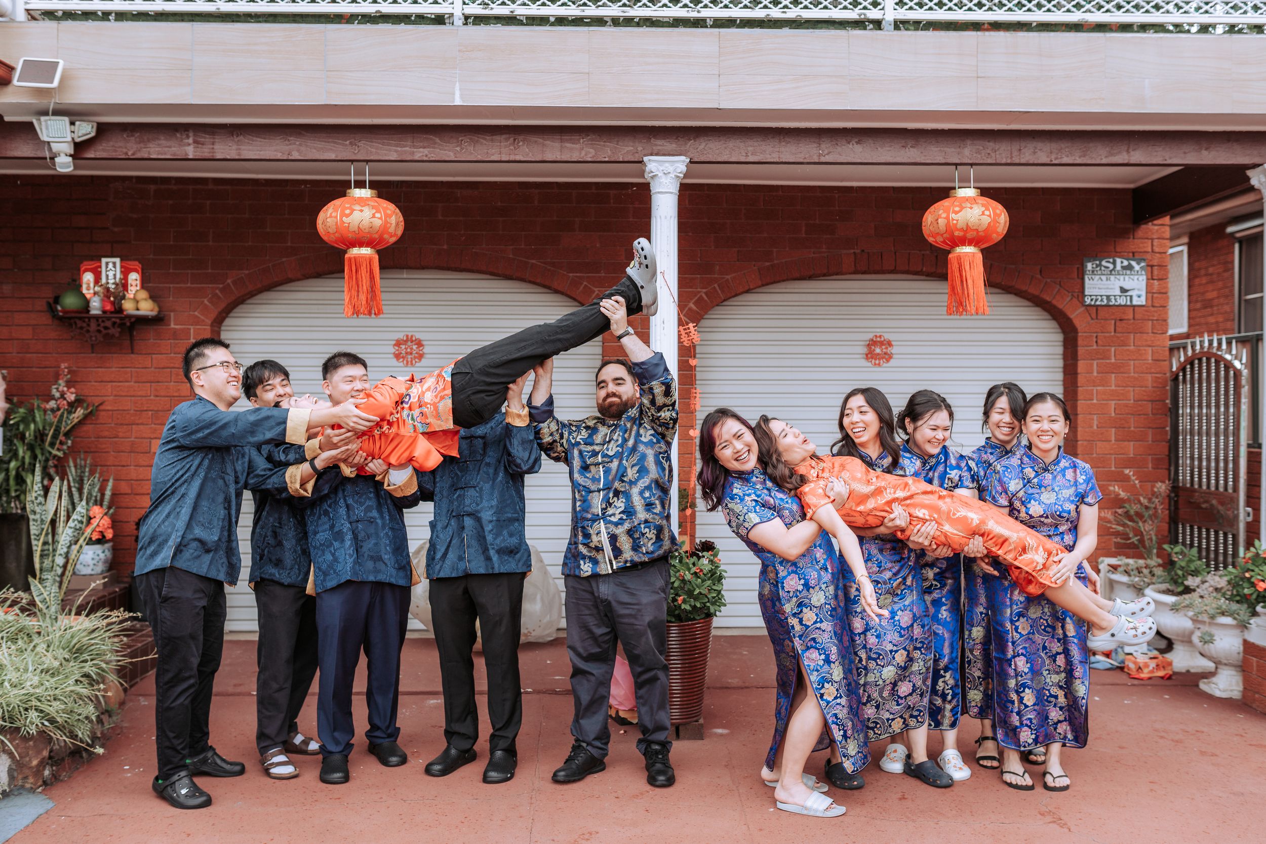Wedding party posing for a fun group photo with traditional Chinese elements and decorations.