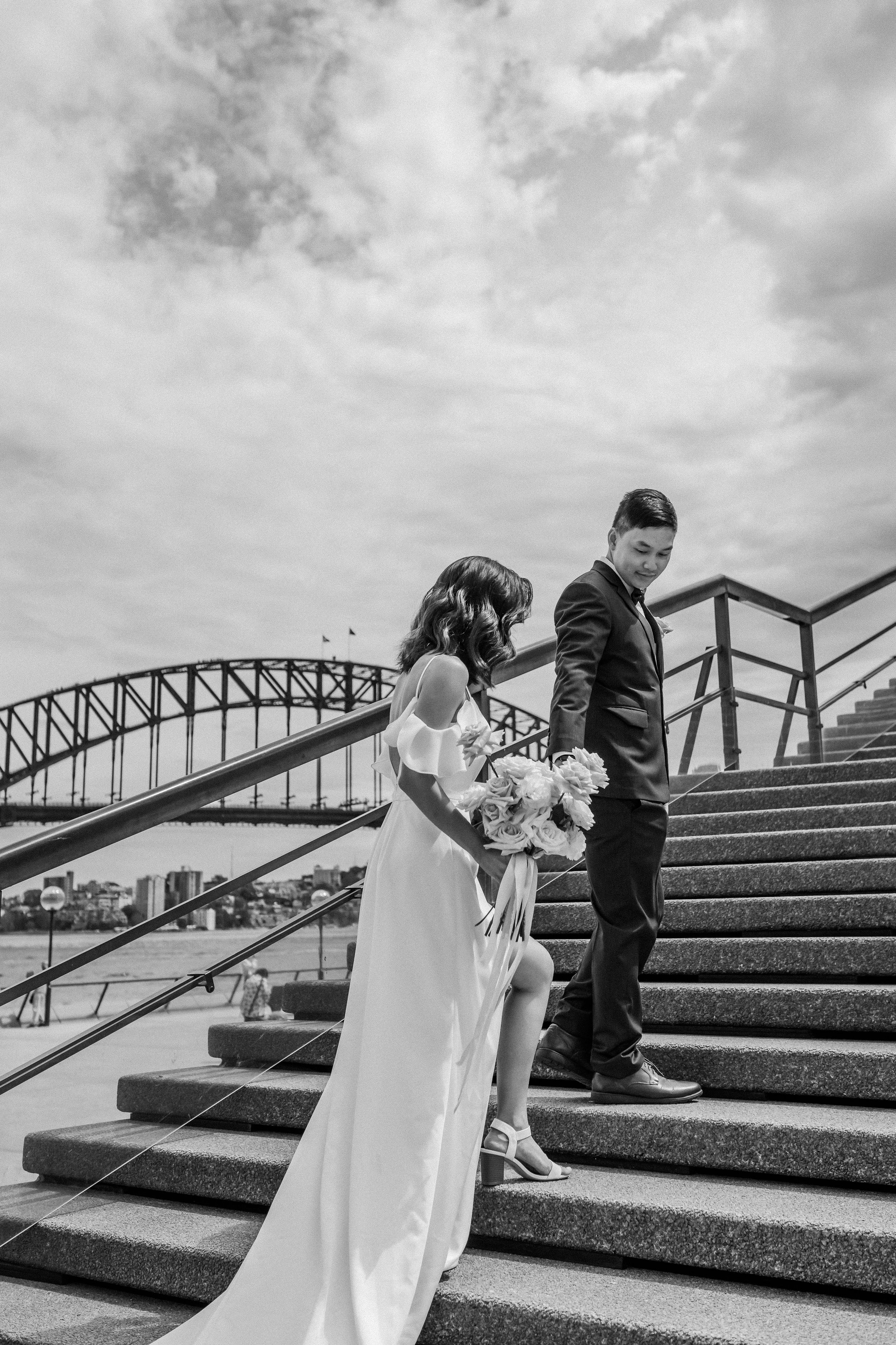 Black and white wedding photo on steps with Sydney Harbour Bridge in background.