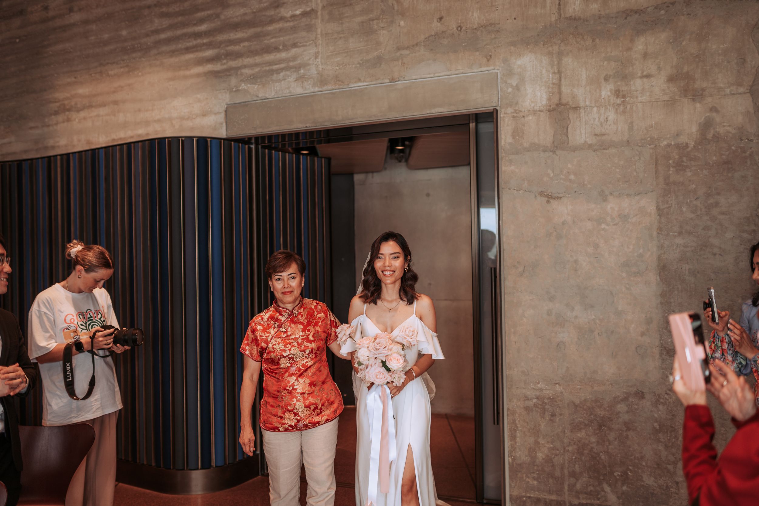 Wedding entrance moment through modern doorway with guests capturing photos.
