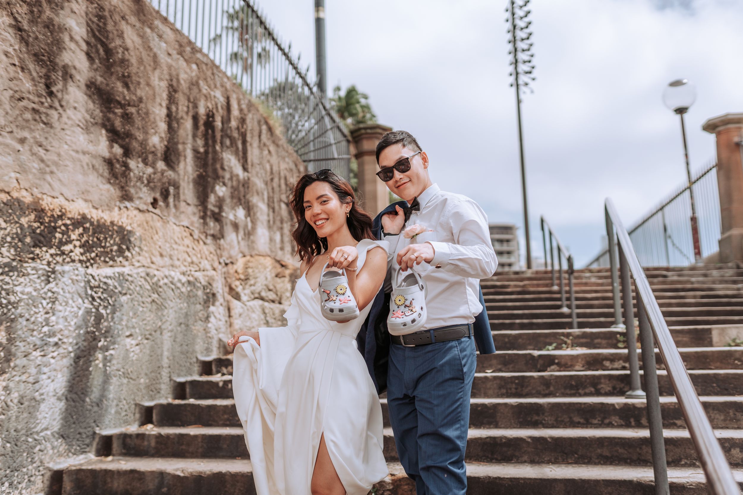A romantic couple poses on stone steps against a weathered wall in elegant attire.