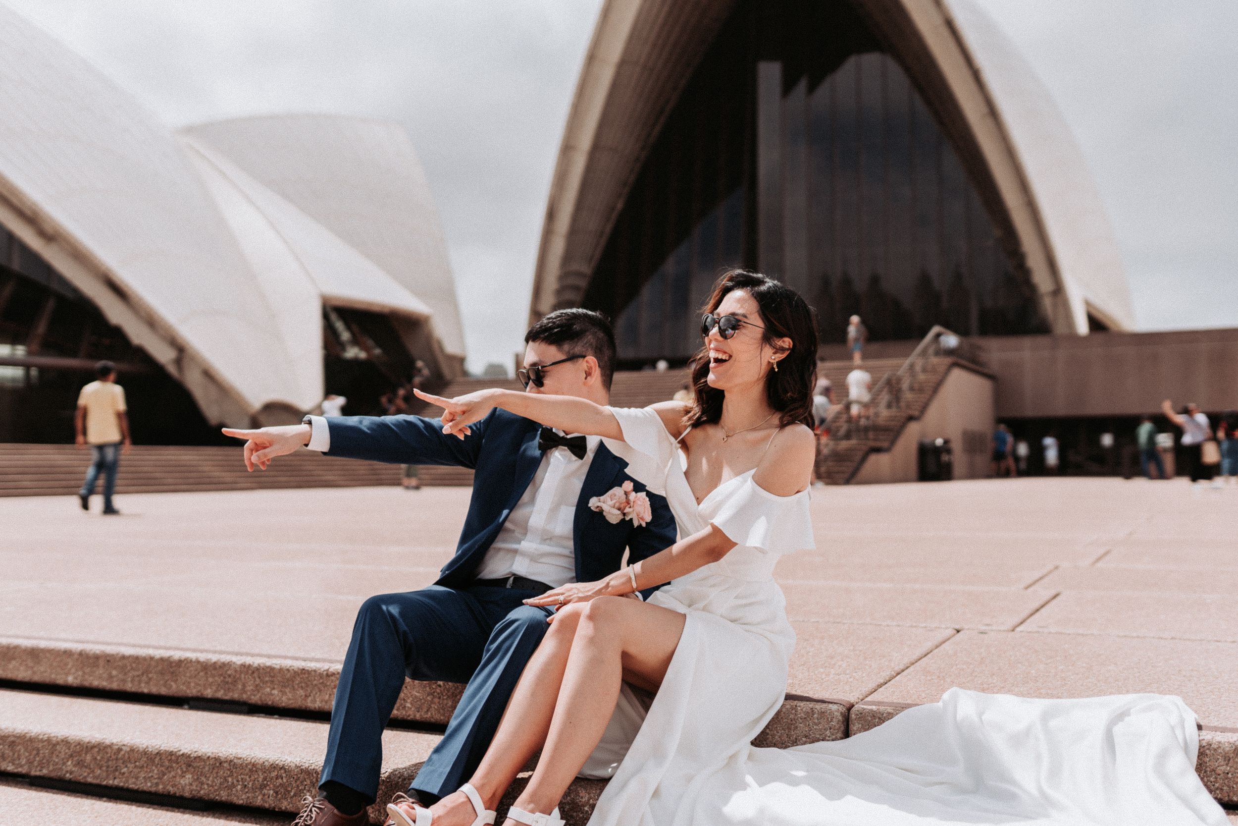 A couple in formal wear shares a playful moment on the steps of the Sydney Opera House.