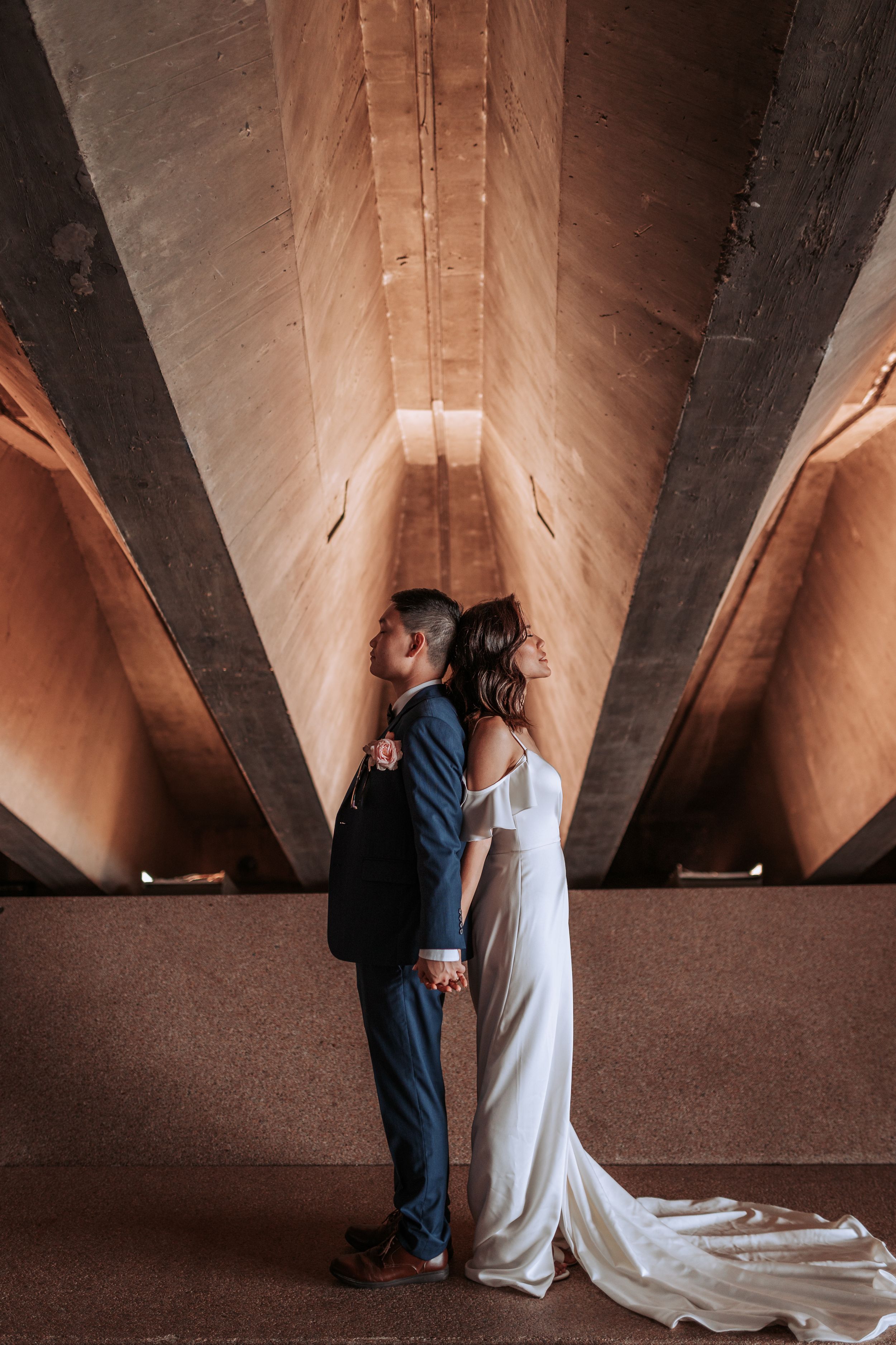 A couple in formal attire poses back-to-back under dramatic architectural angles.