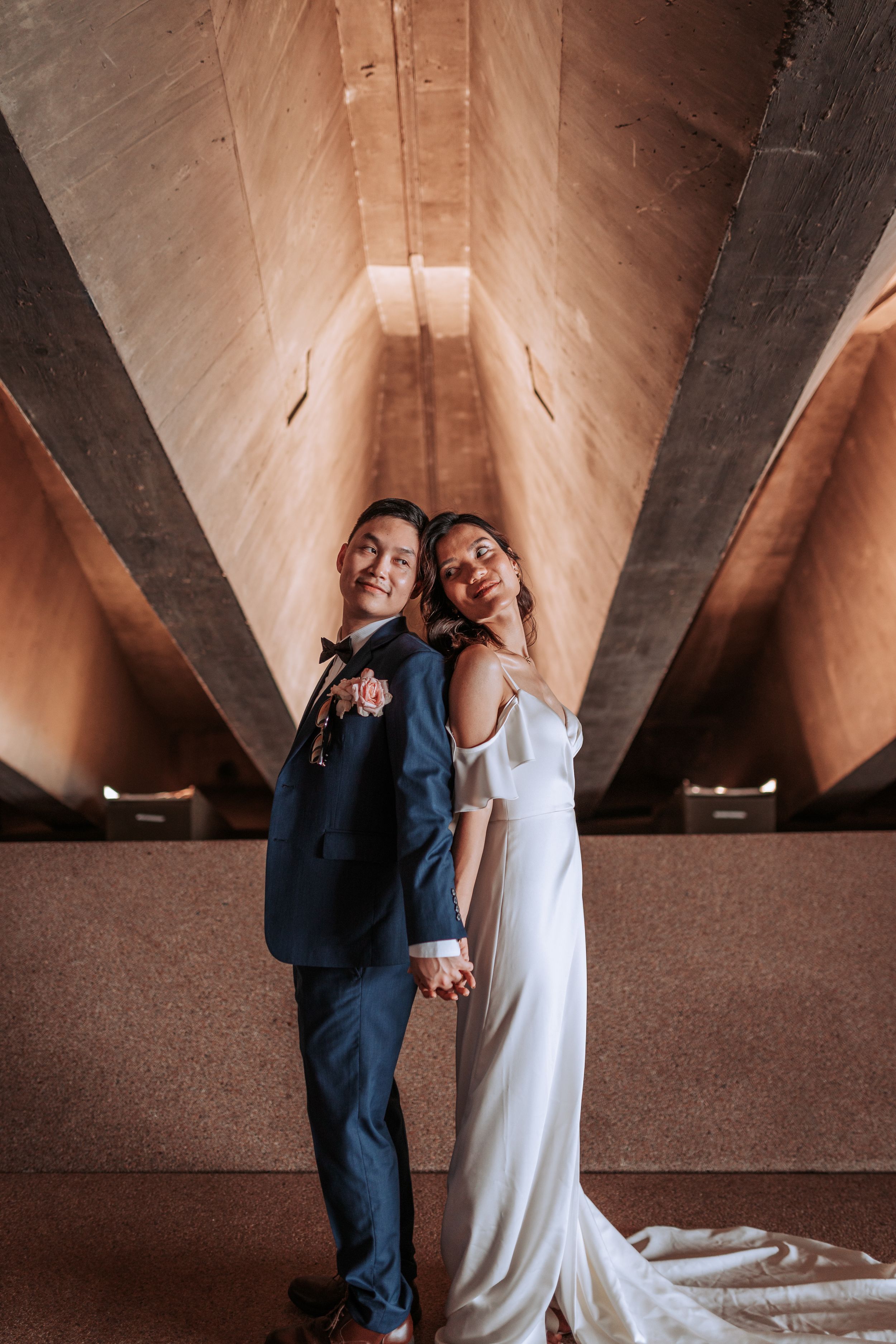 A couple shares a joyful moment under geometric architectural details in formal wear.
