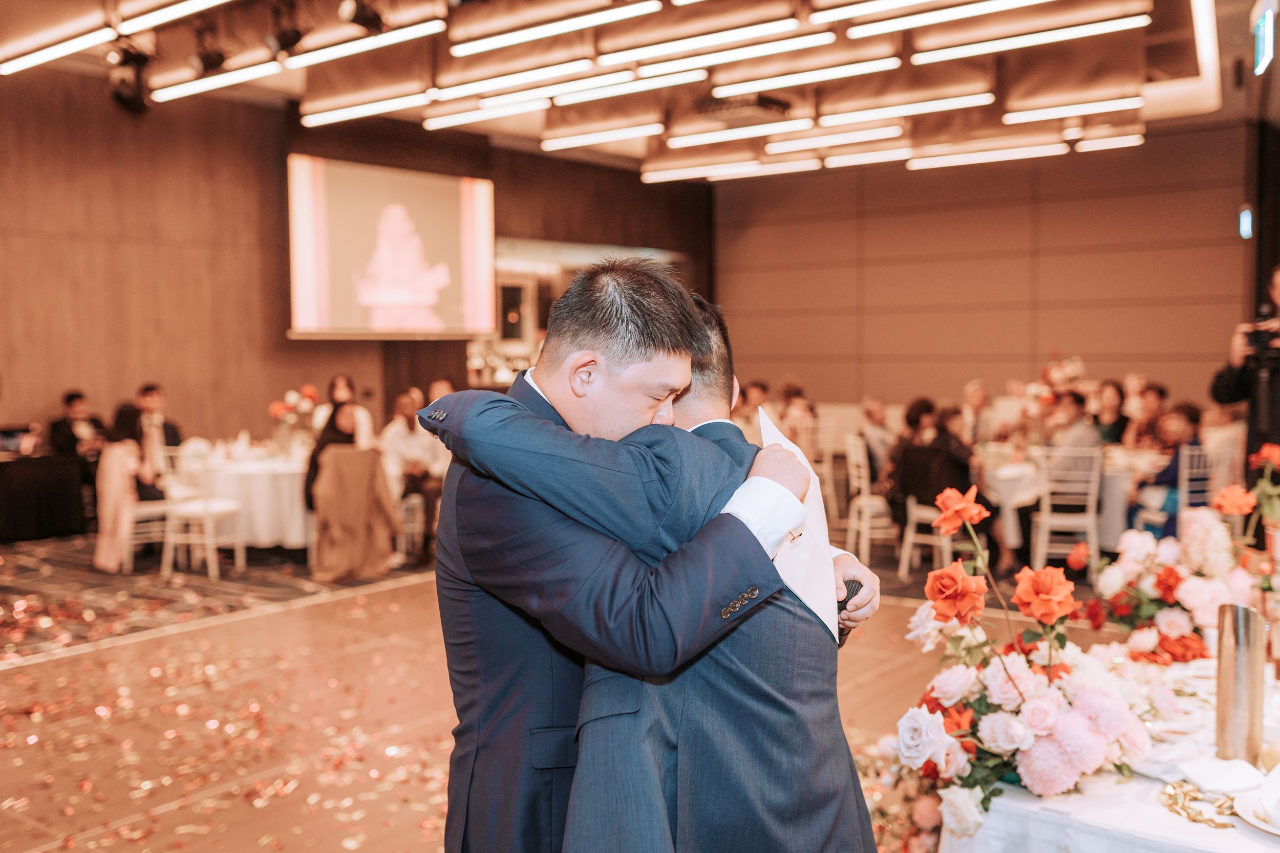 Emotional moment during wedding reception in modern venue with decorative lighting.