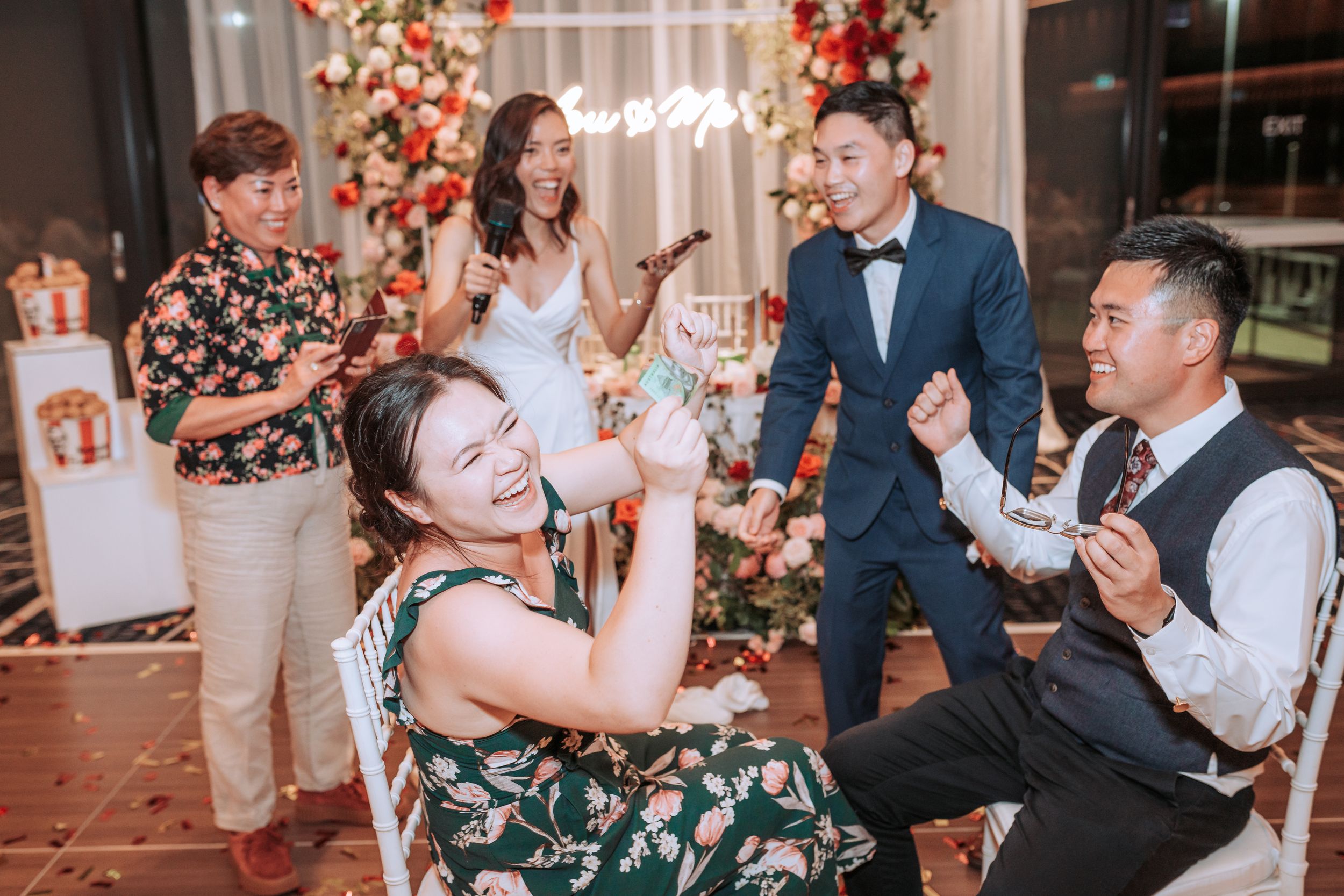 Wedding guests enjoying lively celebration under floral arch with festive lighting.