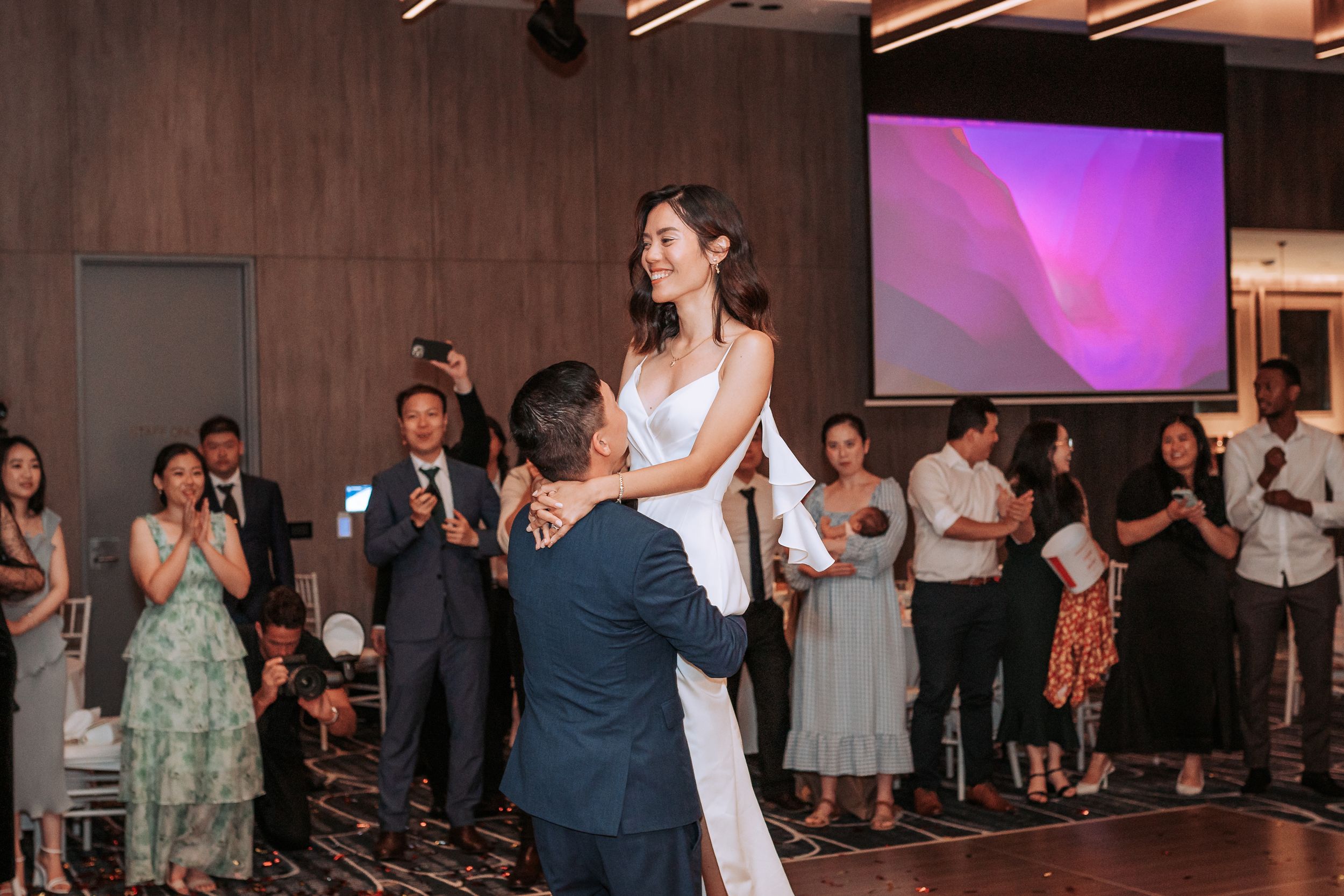 Wedding dance celebration with guests cheering in modern venue with purple ambient lighting.