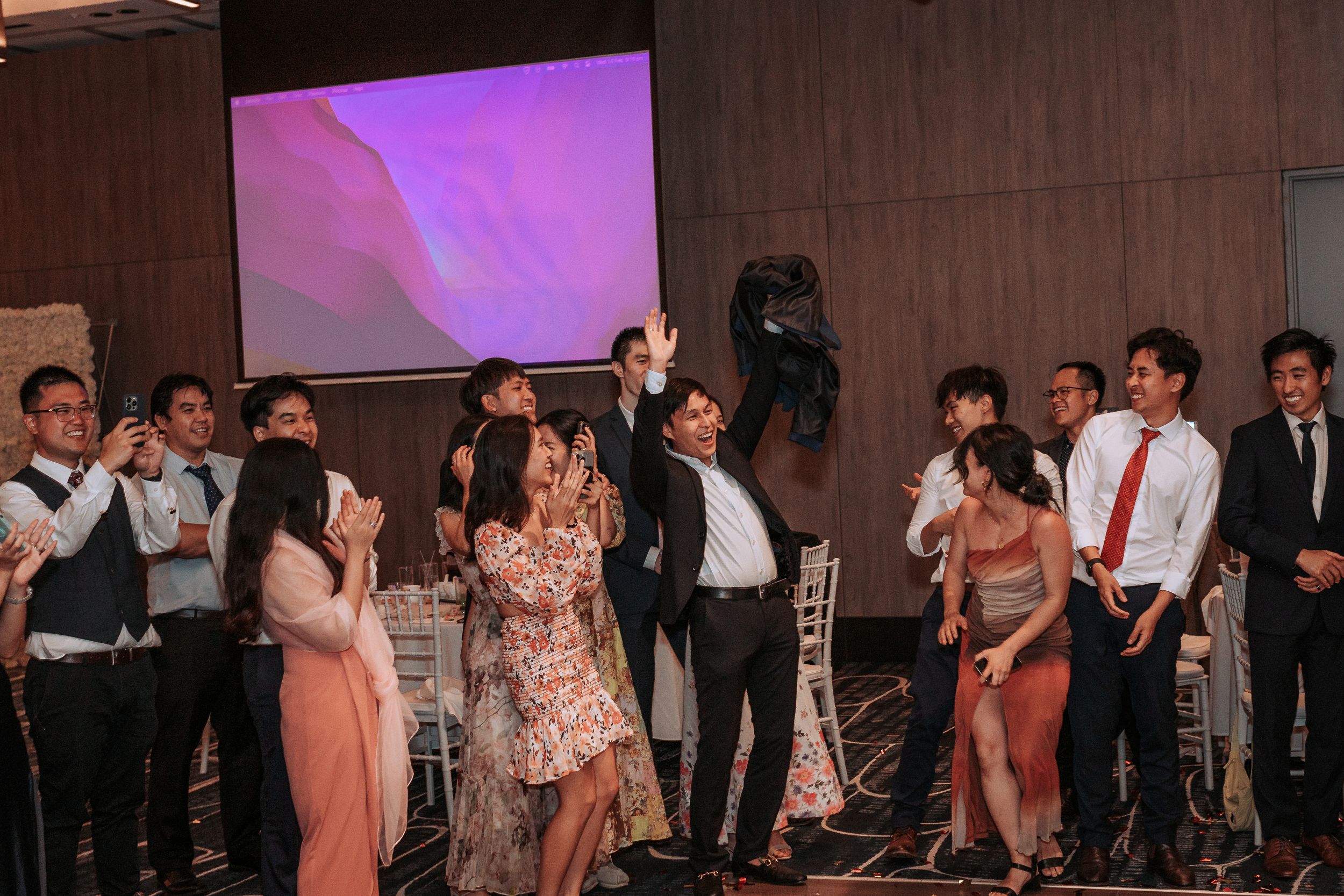 Wedding guests dancing and celebrating on the dance floor with purple lighting in background.