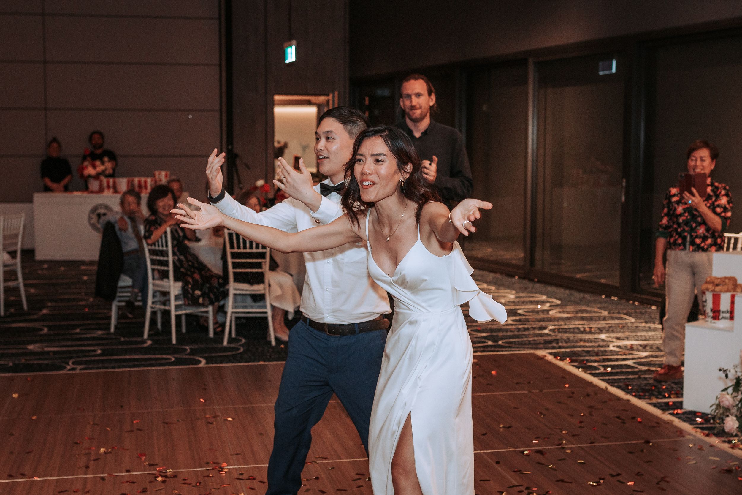 Couple performing energetic dance moves during wedding reception on decorated dance floor.