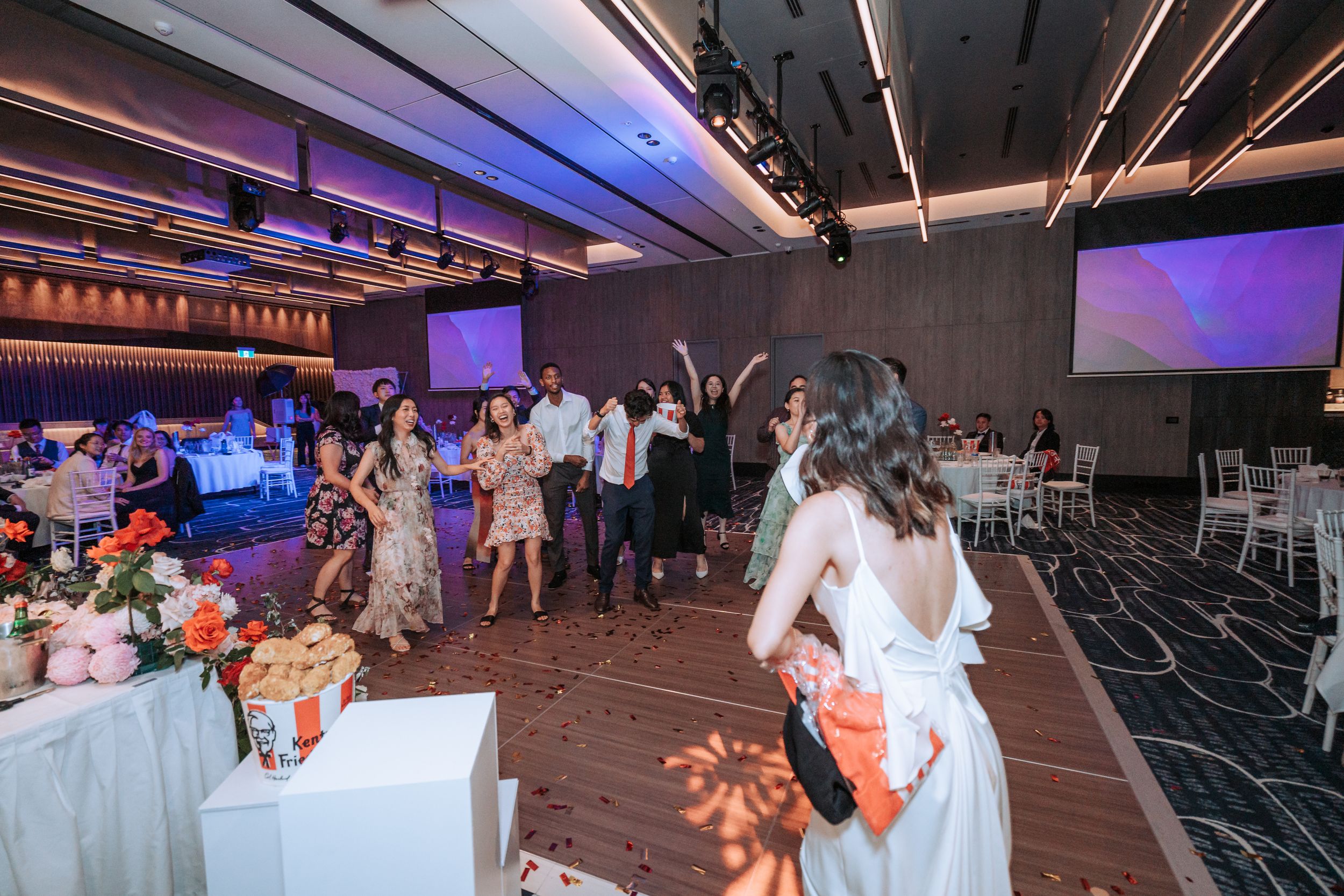 Wedding reception guests dancing and celebrating on a dark dance floor with blue lighting.