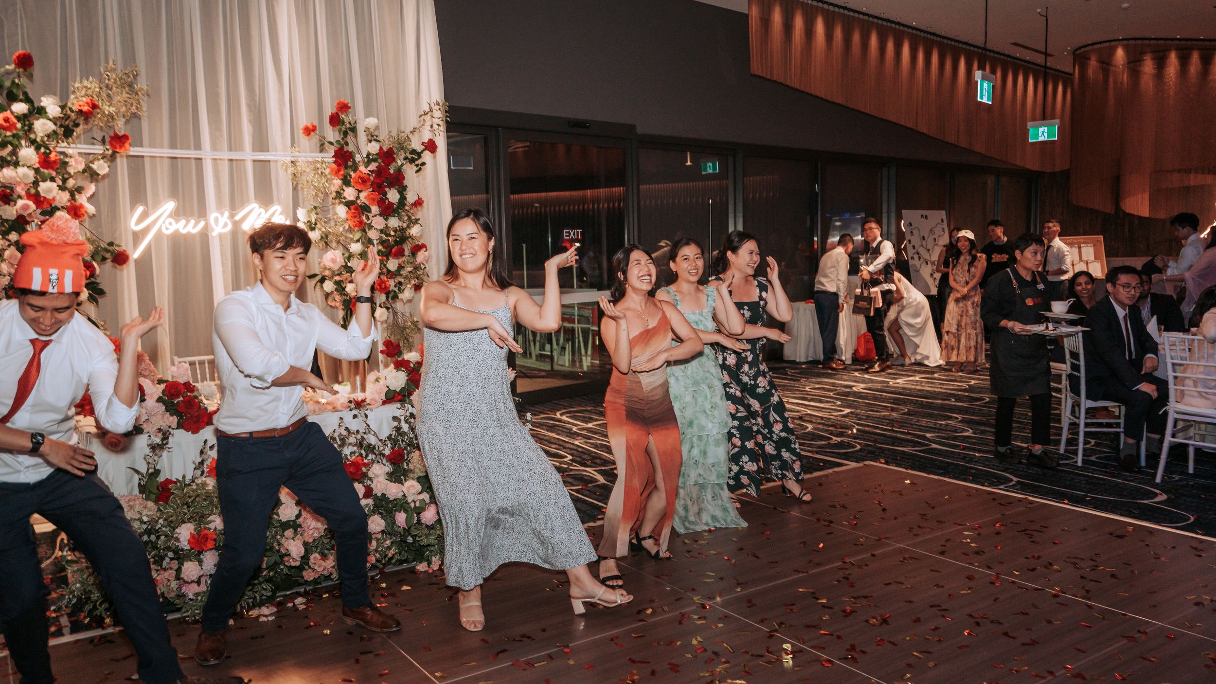 People dancing in formation at a festive event with floral decorations visible.