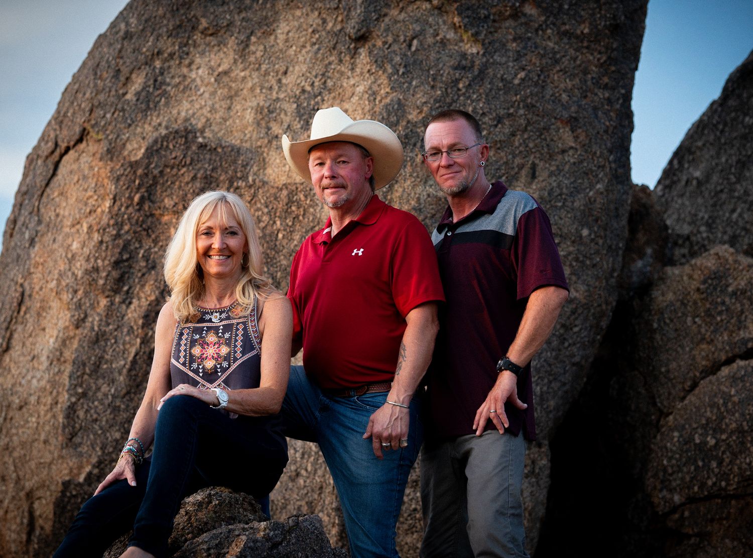 Three friends pose together against large granite boulders during golden hour.
