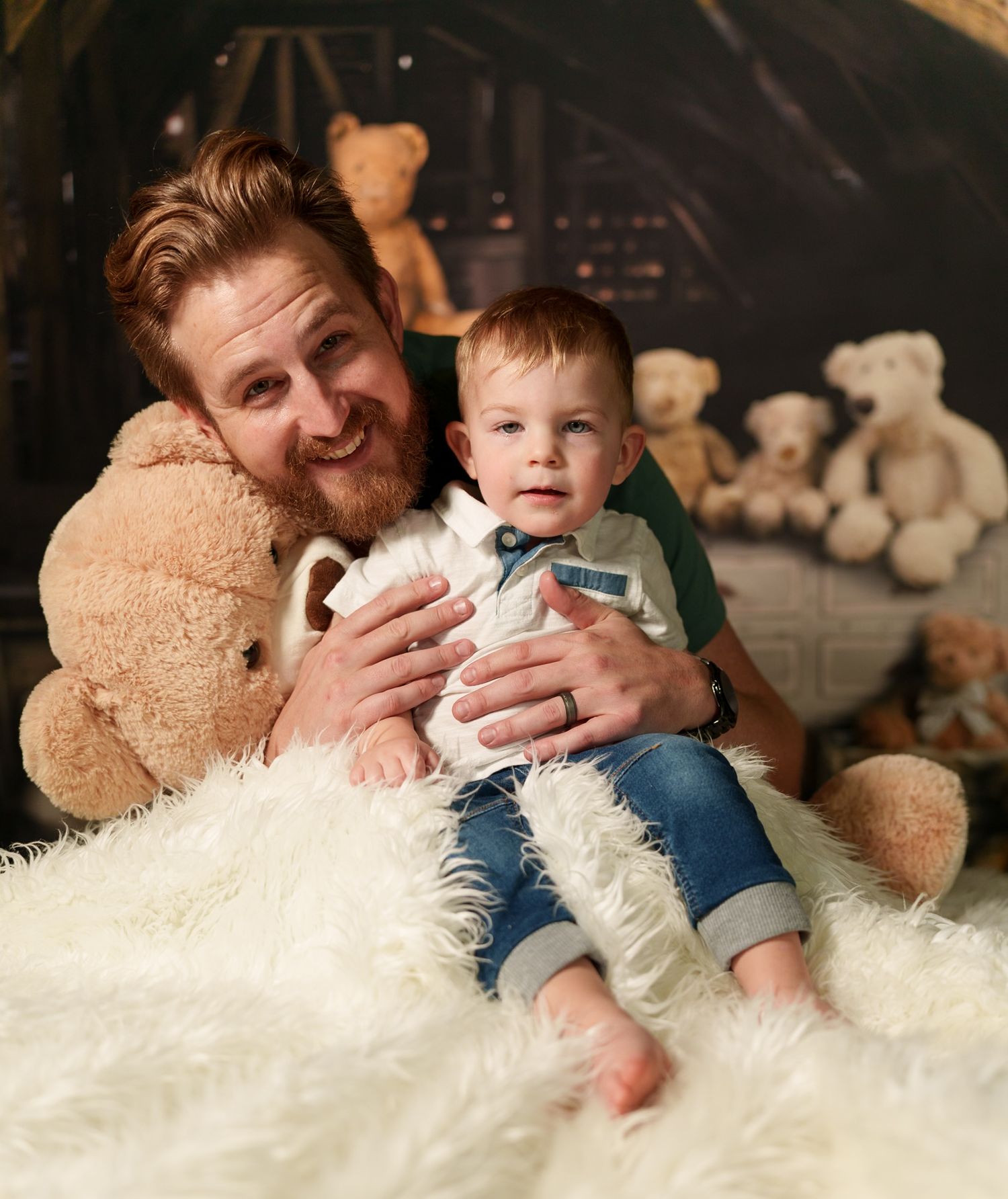 Happy father and child sit together on plush white rug with teddy bears in background.