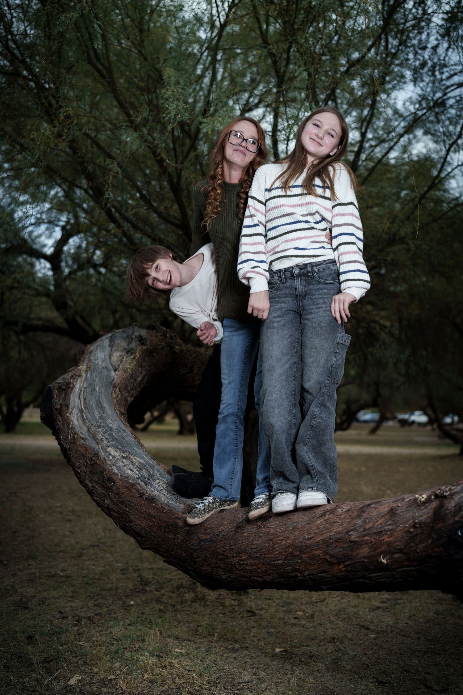 Two friends enjoying a playful moment while standing on a curved tree branch in a park setting.