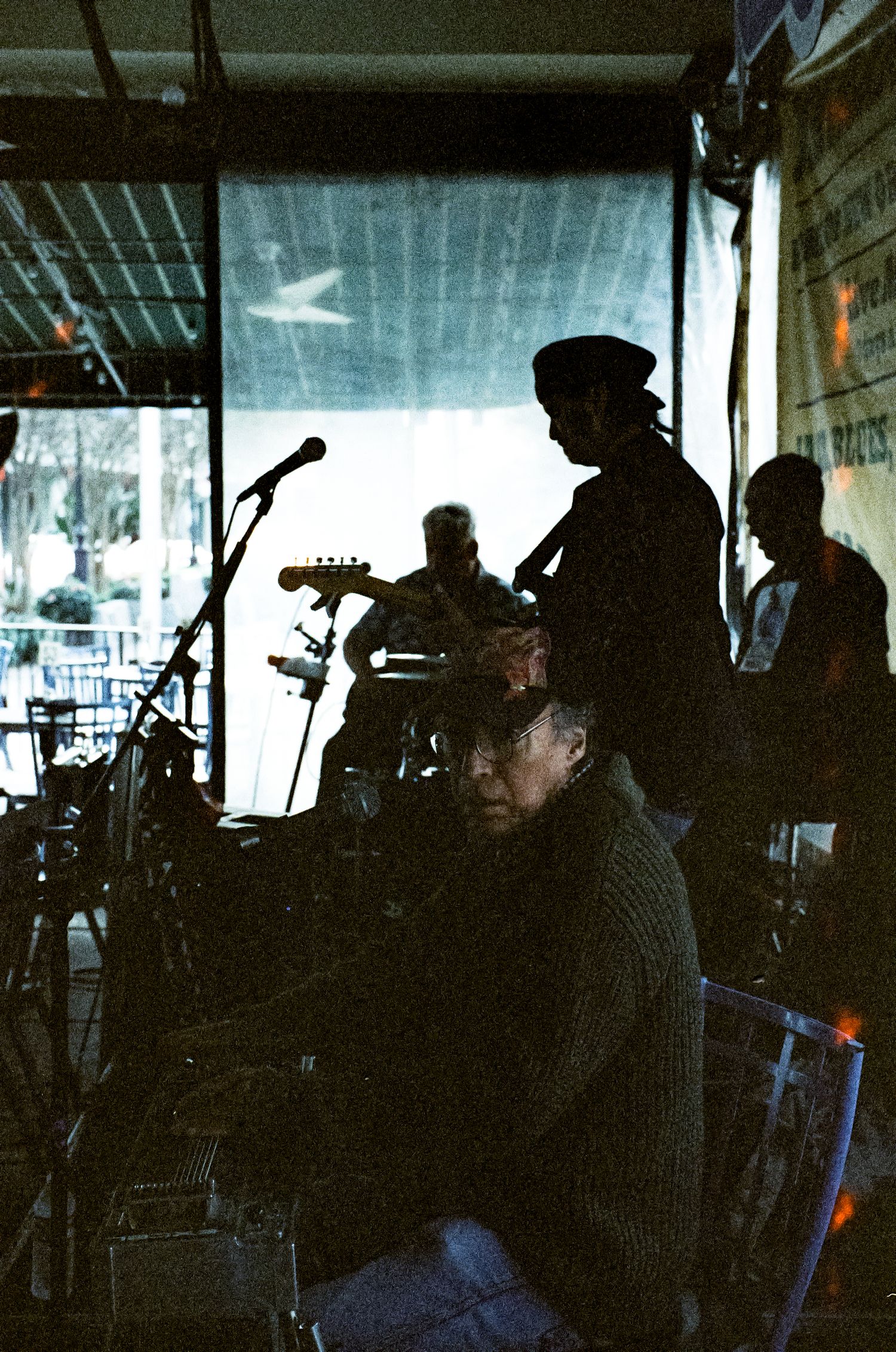 Silhouetted musicians perform on a dimly lit stage with instruments and microphones visible.
