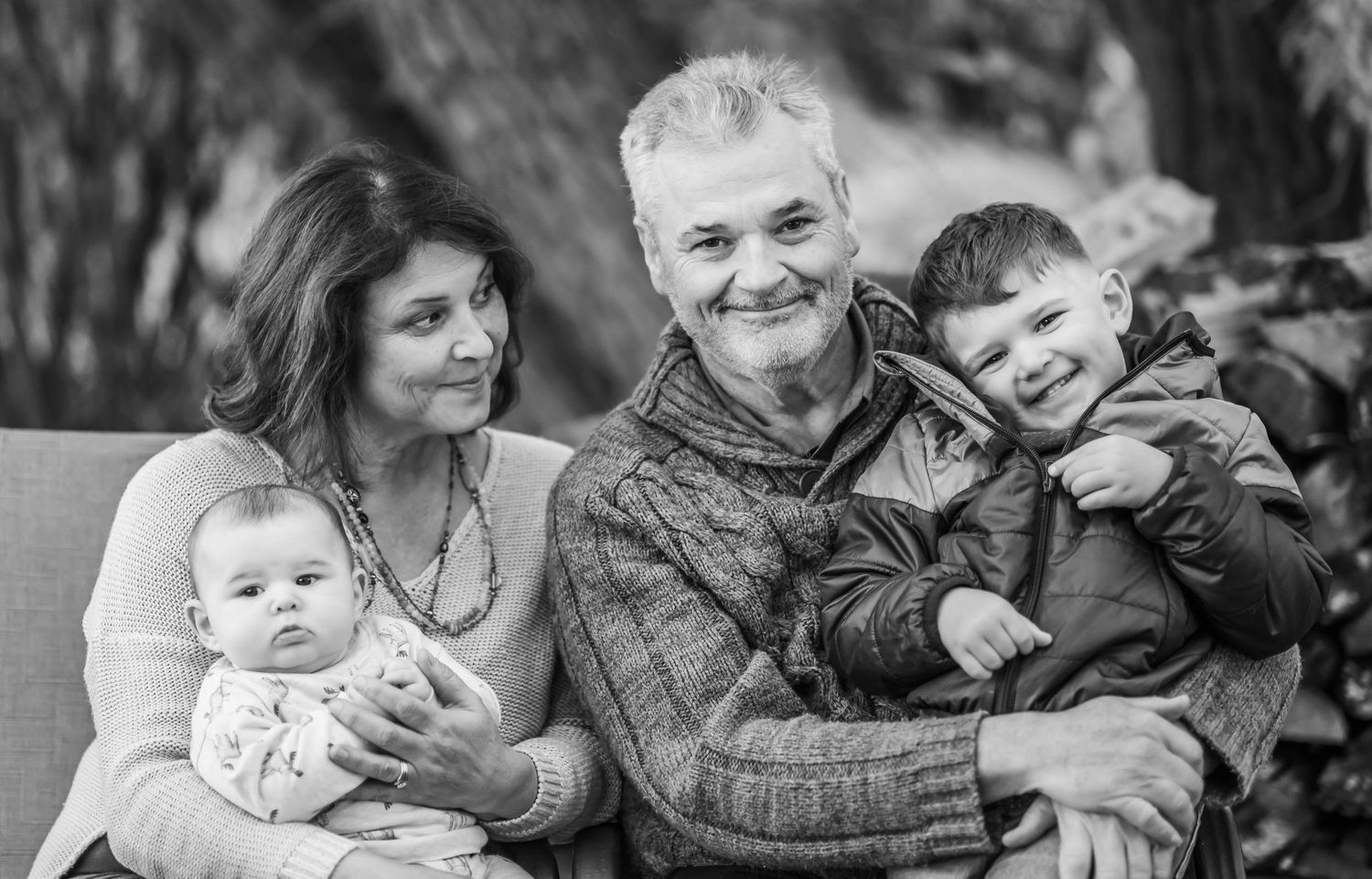 Black and white portrait of a family group sitting together on a couch outdoors.
