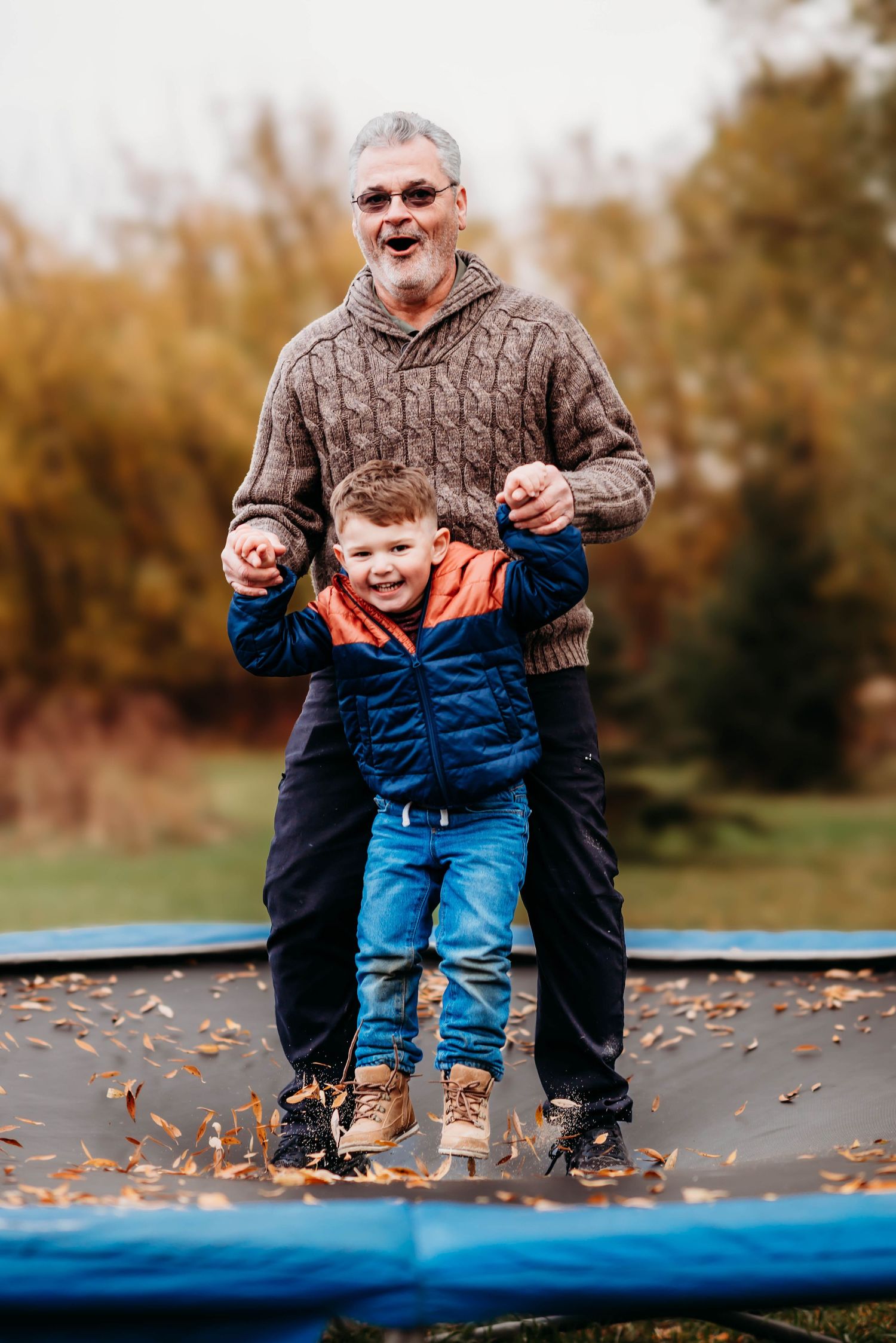 Adult and child playfully sitting together on blue equipment at a park on an autumn day with fallen leaves around them.