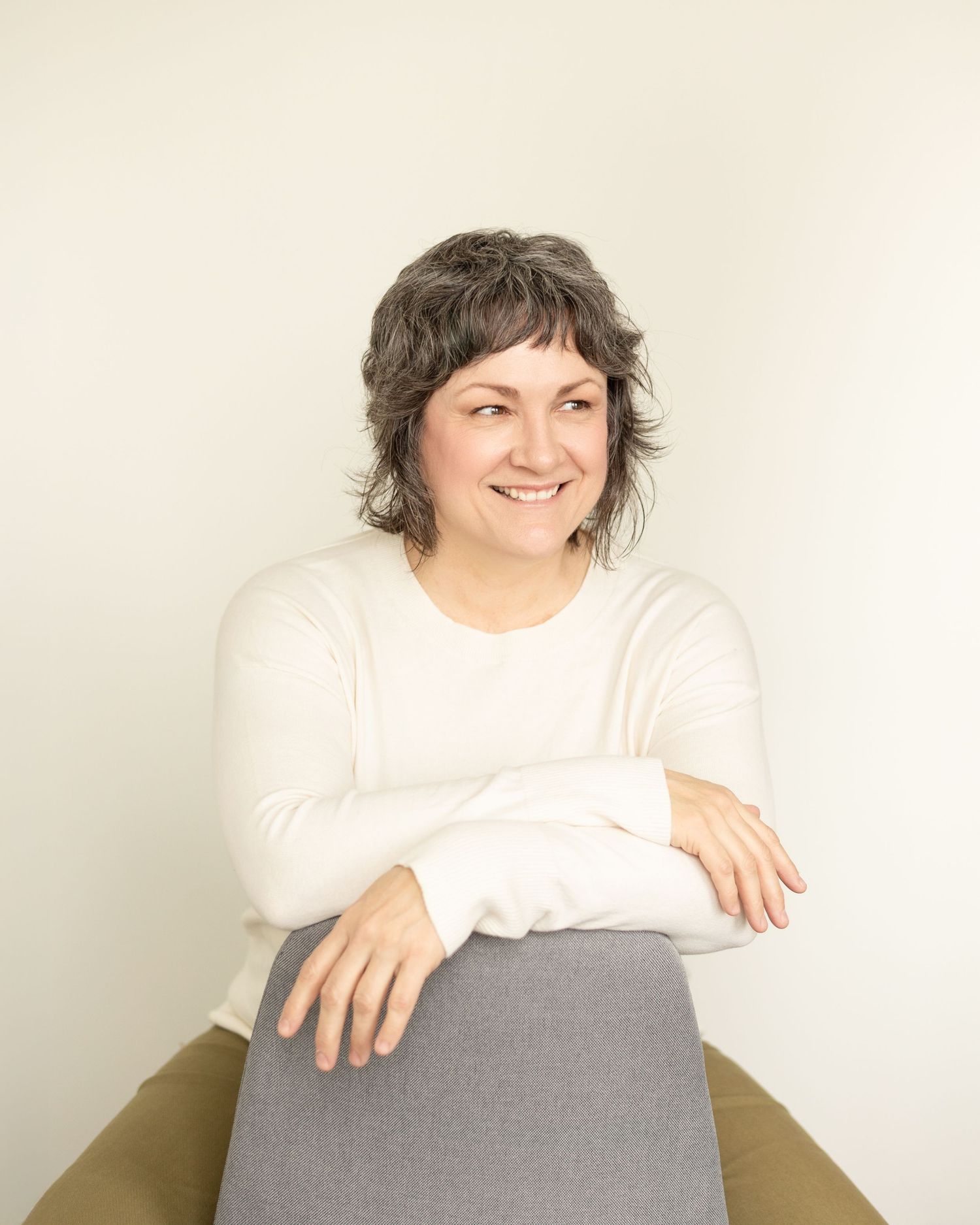 Personal branding portrait of a healing arts therapist woman Nancy Dougherty from Niagara in a white top, smiling warmly with arms crossed.