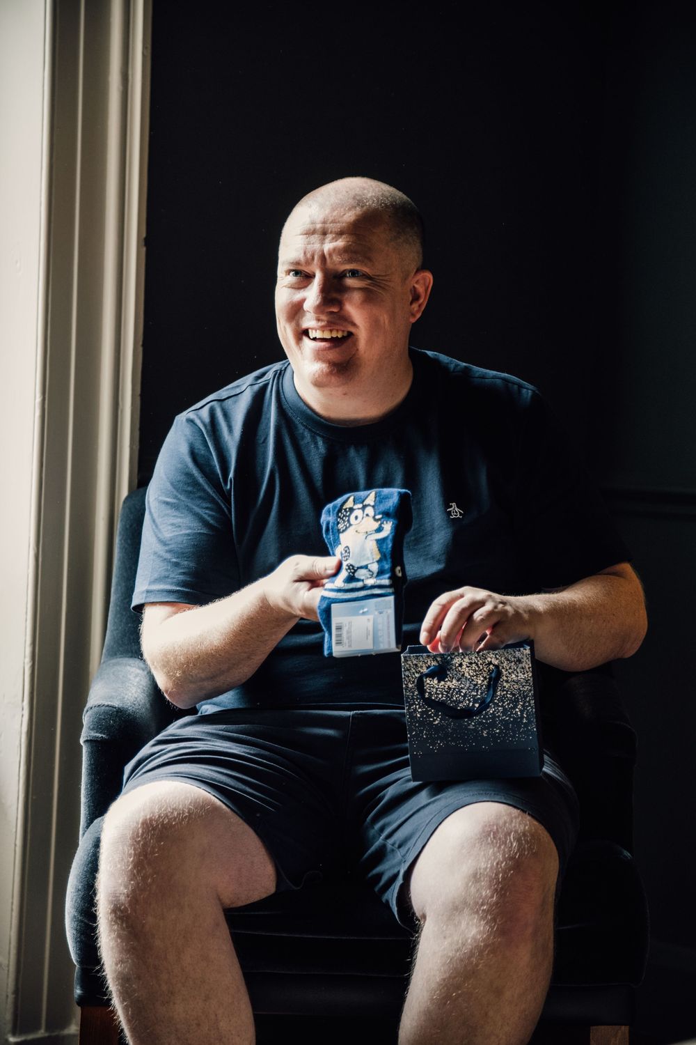 Person in dark shirt sitting casually while holding something in their hands.
