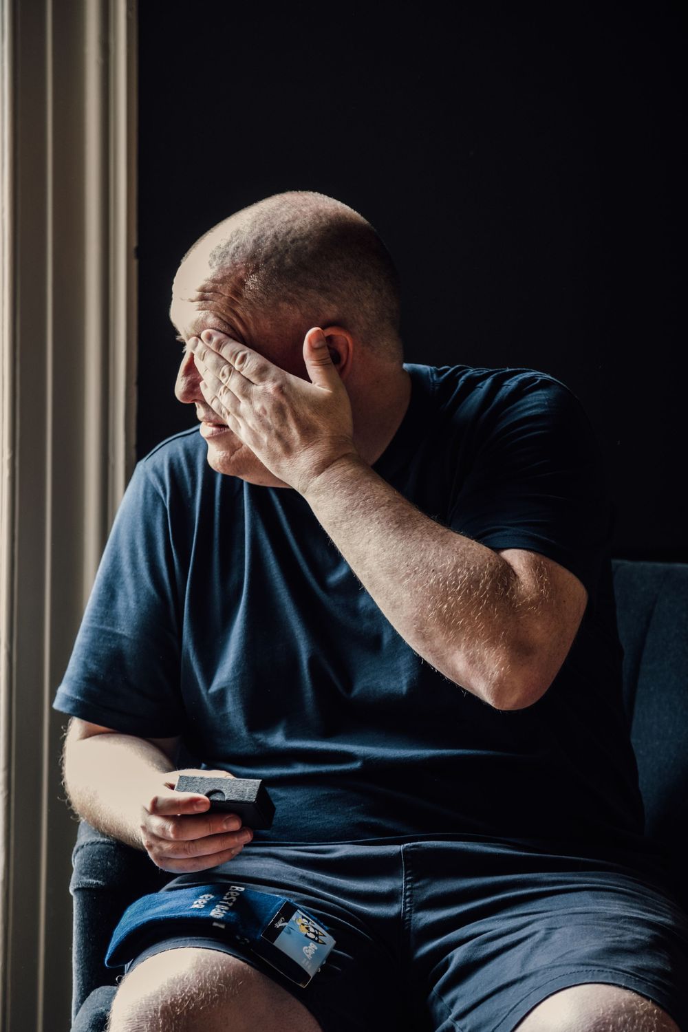 Person in navy blue shirt sitting by window looking at phone.
