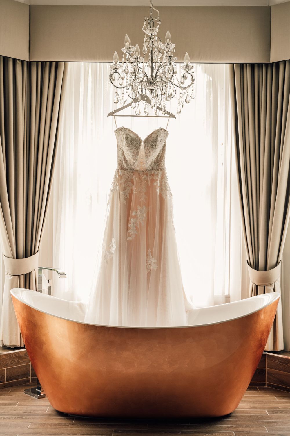 Copper bathtub in an elegant room with hanging wedding dress and chandelier.