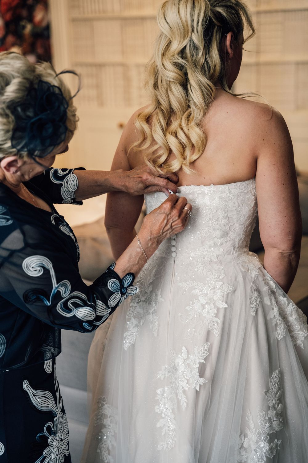 Close-up shots of someone adjusting the back of an ornate white lace wedding dress.