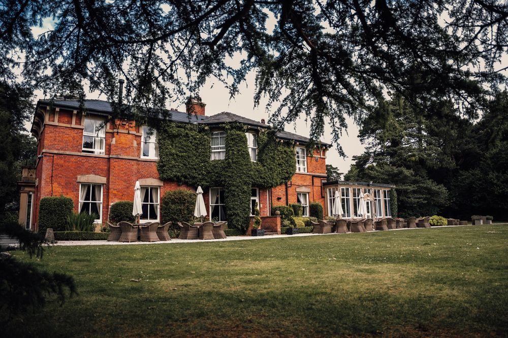 Panoramic view of a red brick manor house with manicured lawn and trees.