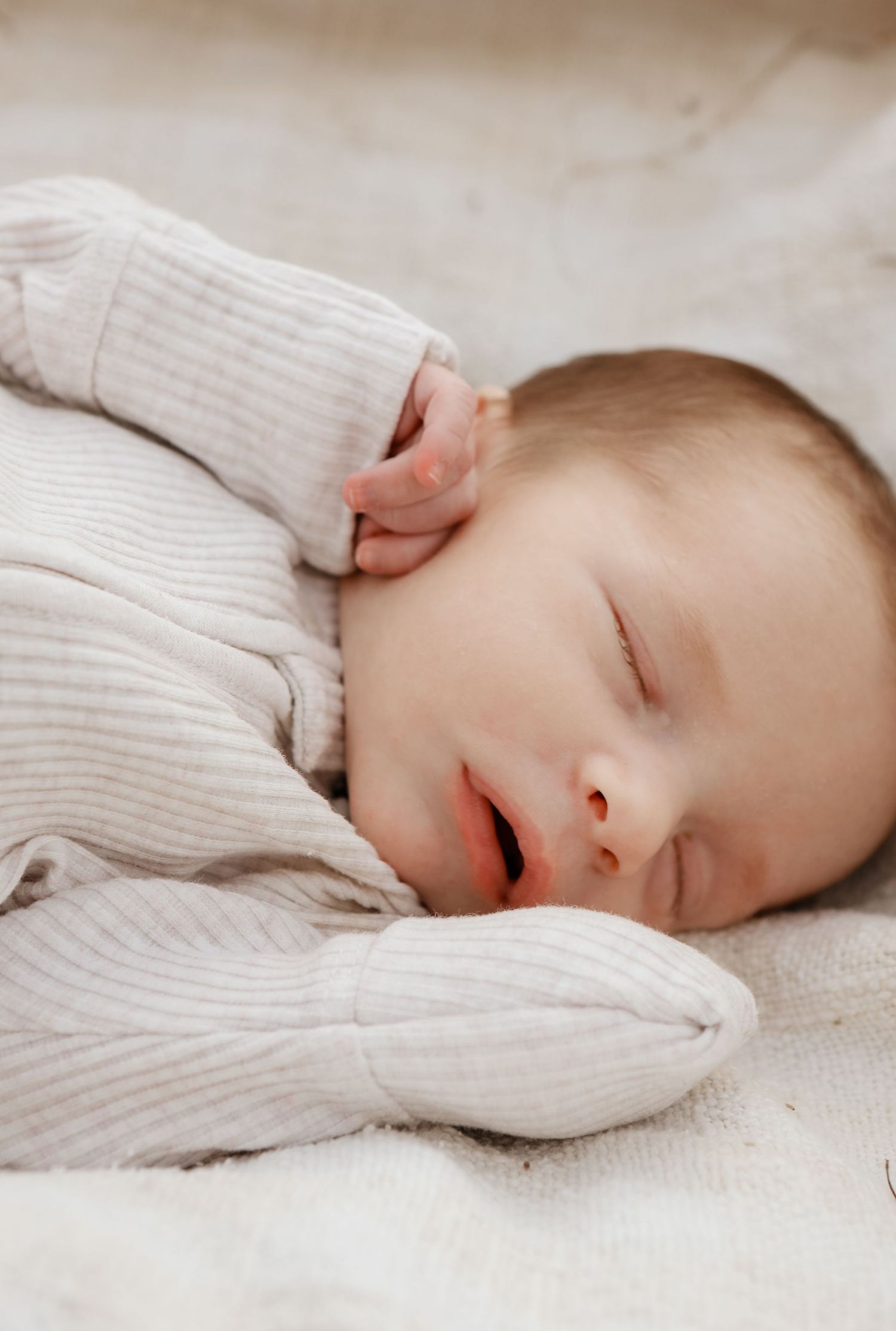 A peaceful sleeping baby in a cozy cream-colored knit sweater rests on soft white bedding.
