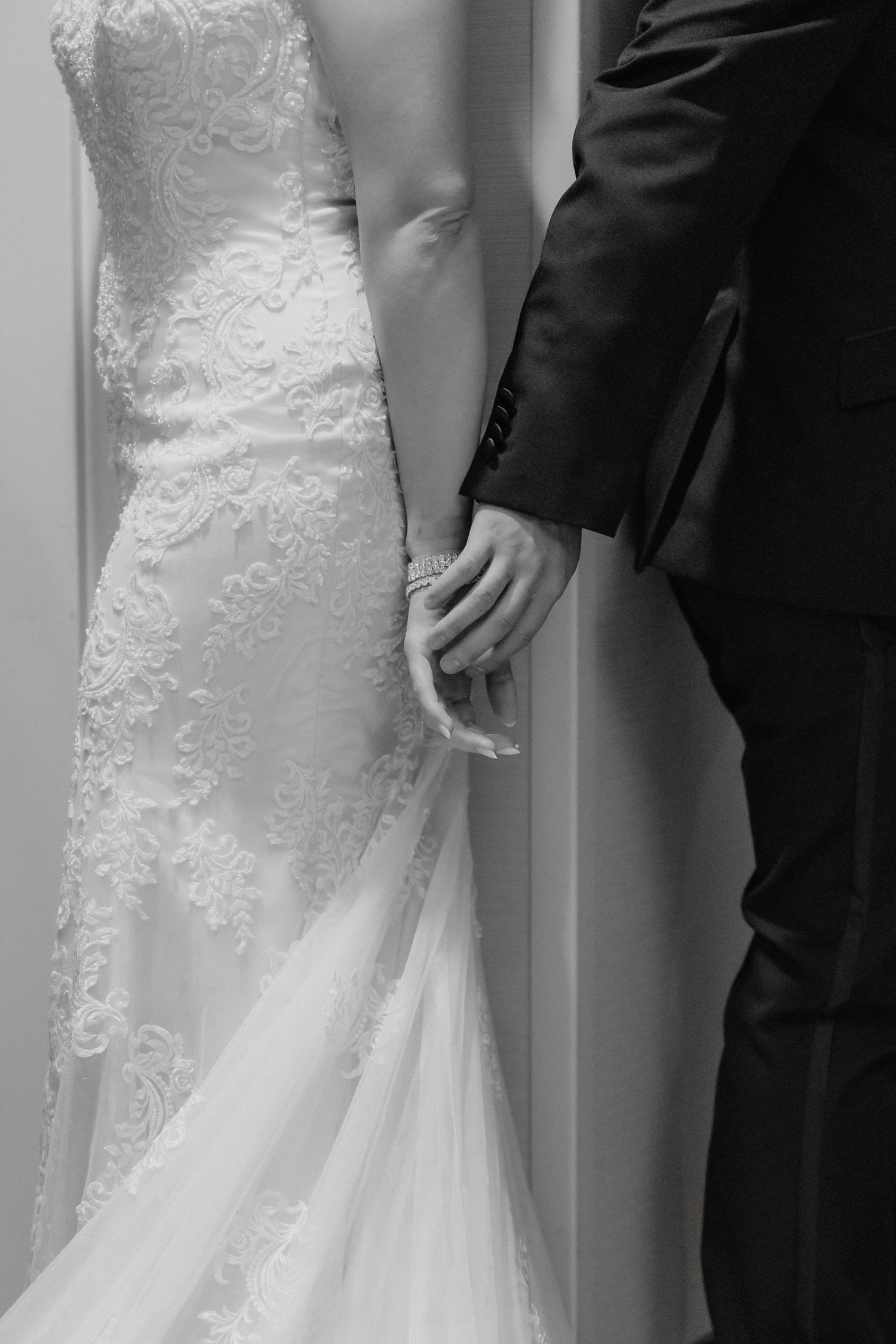 Wedding couple showing dress details with intricate lace and fitted bodice against warm-toned lighting.