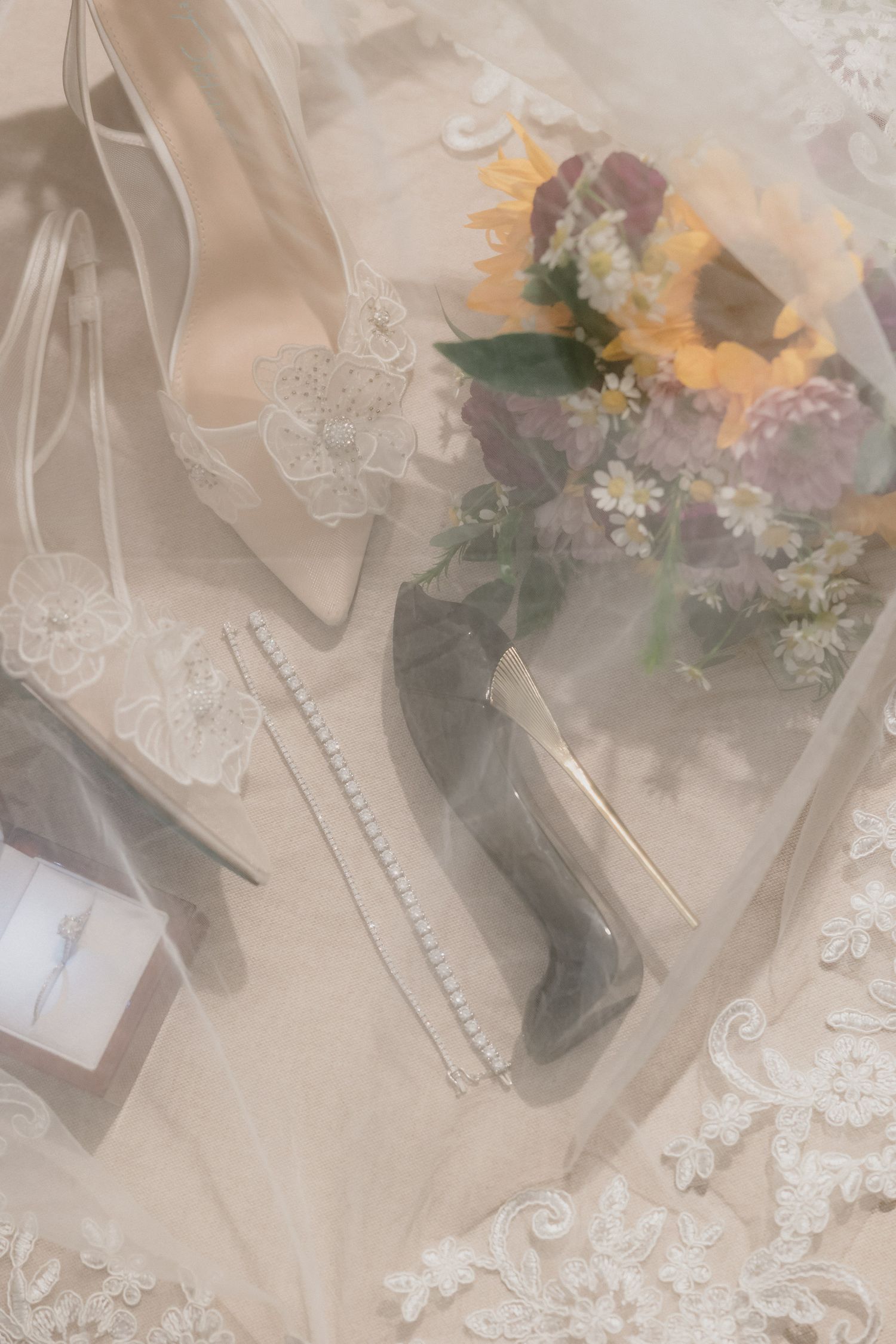 Close up view of sheer cream colored lace fabric with artificial flowers and floral embellishments arranged on a surface.
