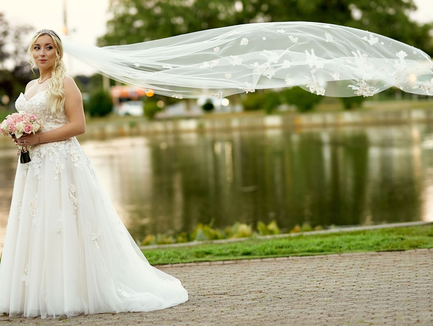 Bride's veil flows dramatically in the breeze by a waterfront setting.