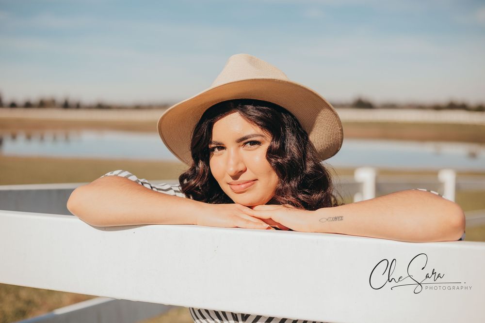 Portrait of person in brown hat leaning on white fence with soft lighting.