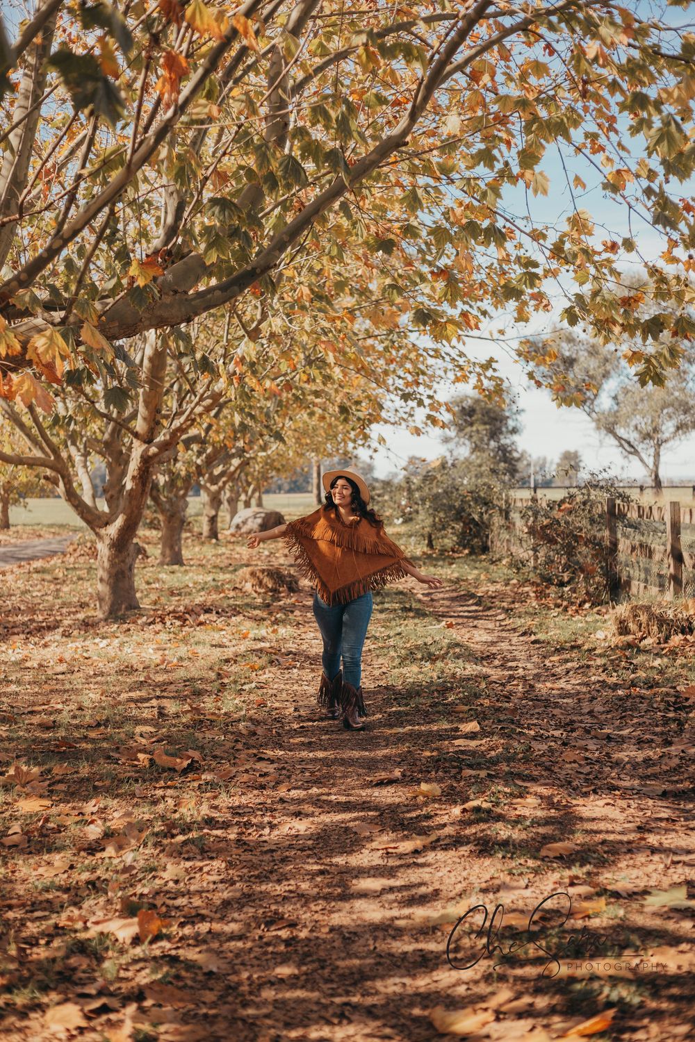 Person in brown sweater walking through autumn trees with fallen leaves.