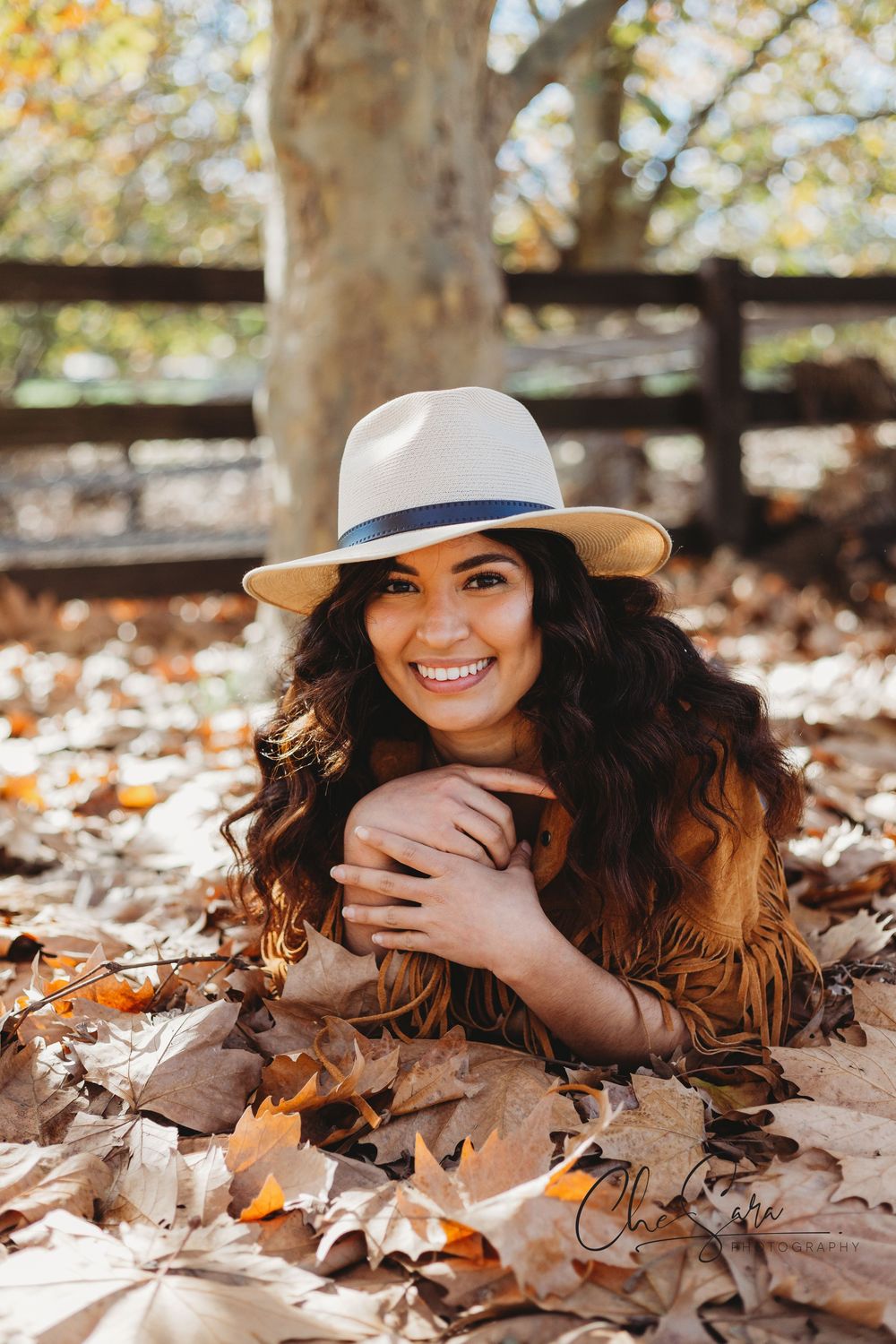 Autumn portrait with person lying in fallen leaves wearing hat and brown sweater.