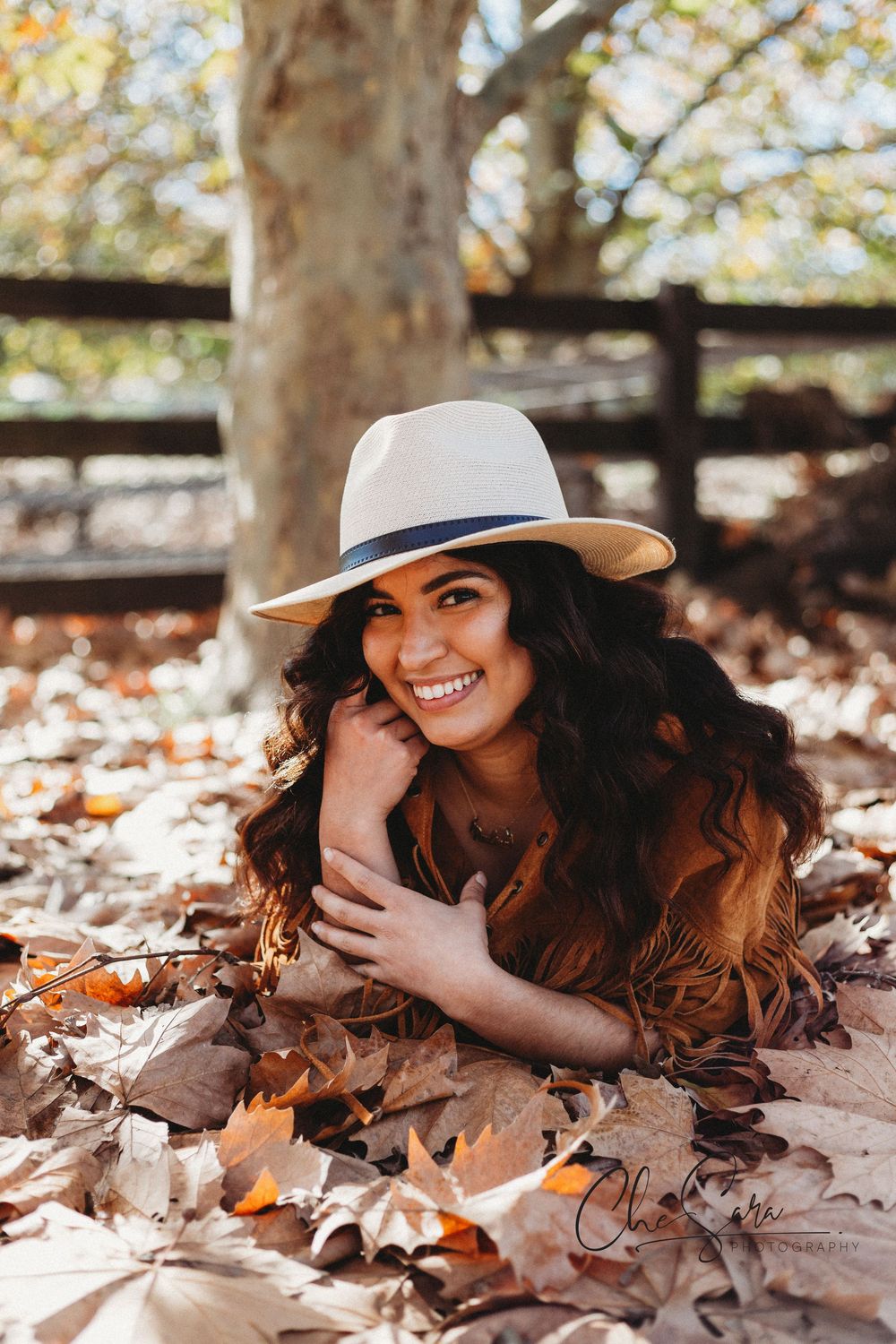 Woman in white hat lying playfully in autumn leaves during outdoor portrait session.