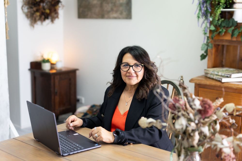 Professional woman working on laptop at home office desk with plants and decor.