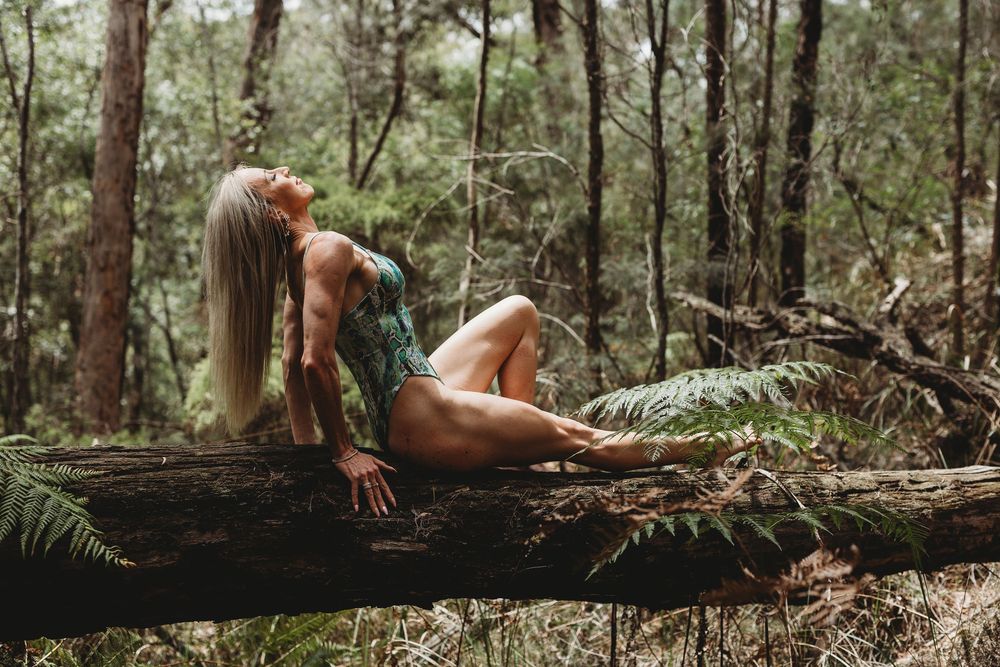 Model in artistic forest photoshoot lying on fallen tree trunk.